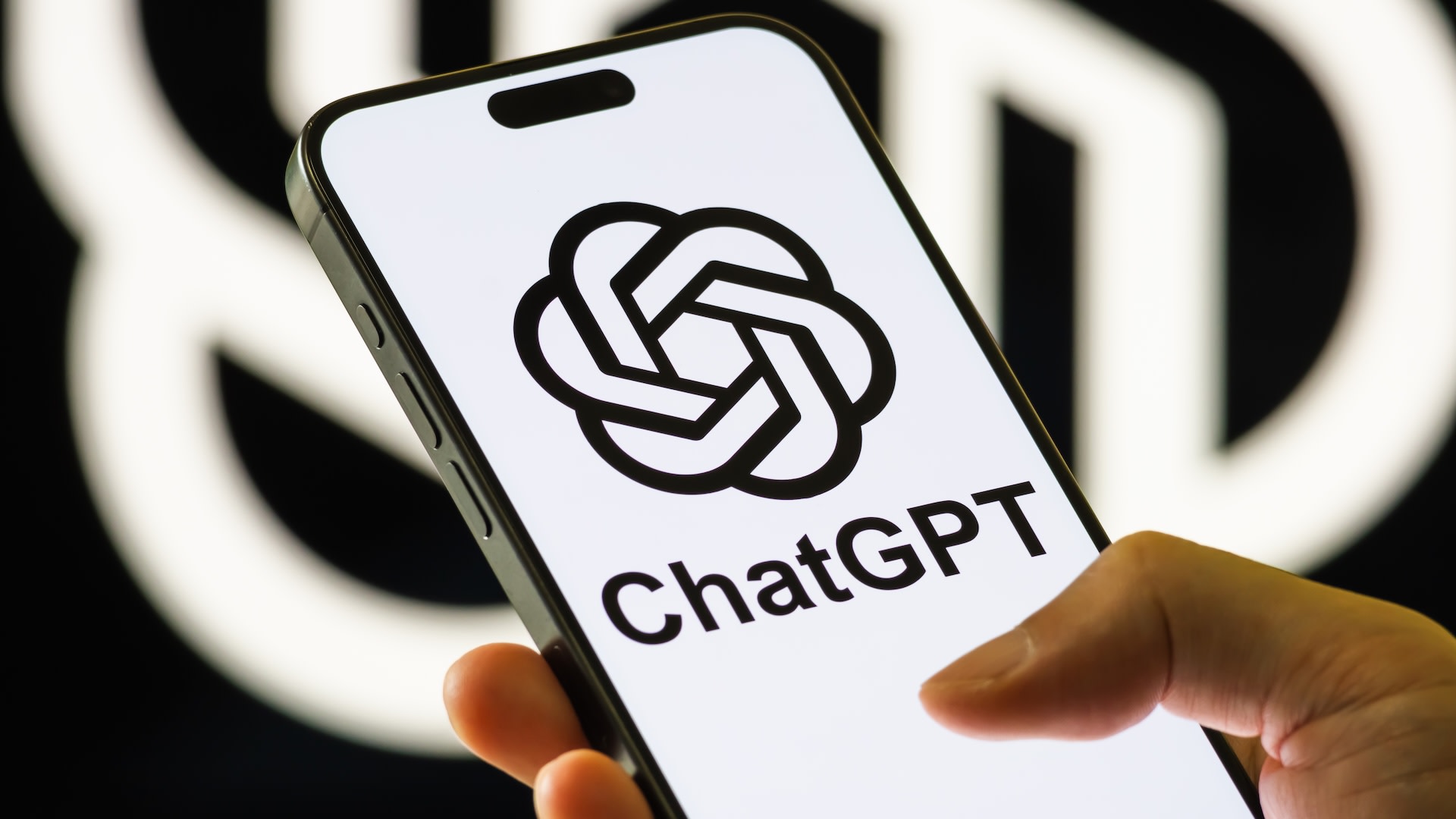 A hand holding a smartphone displaying the ChatGPT logo on the screen, with a blurred background.