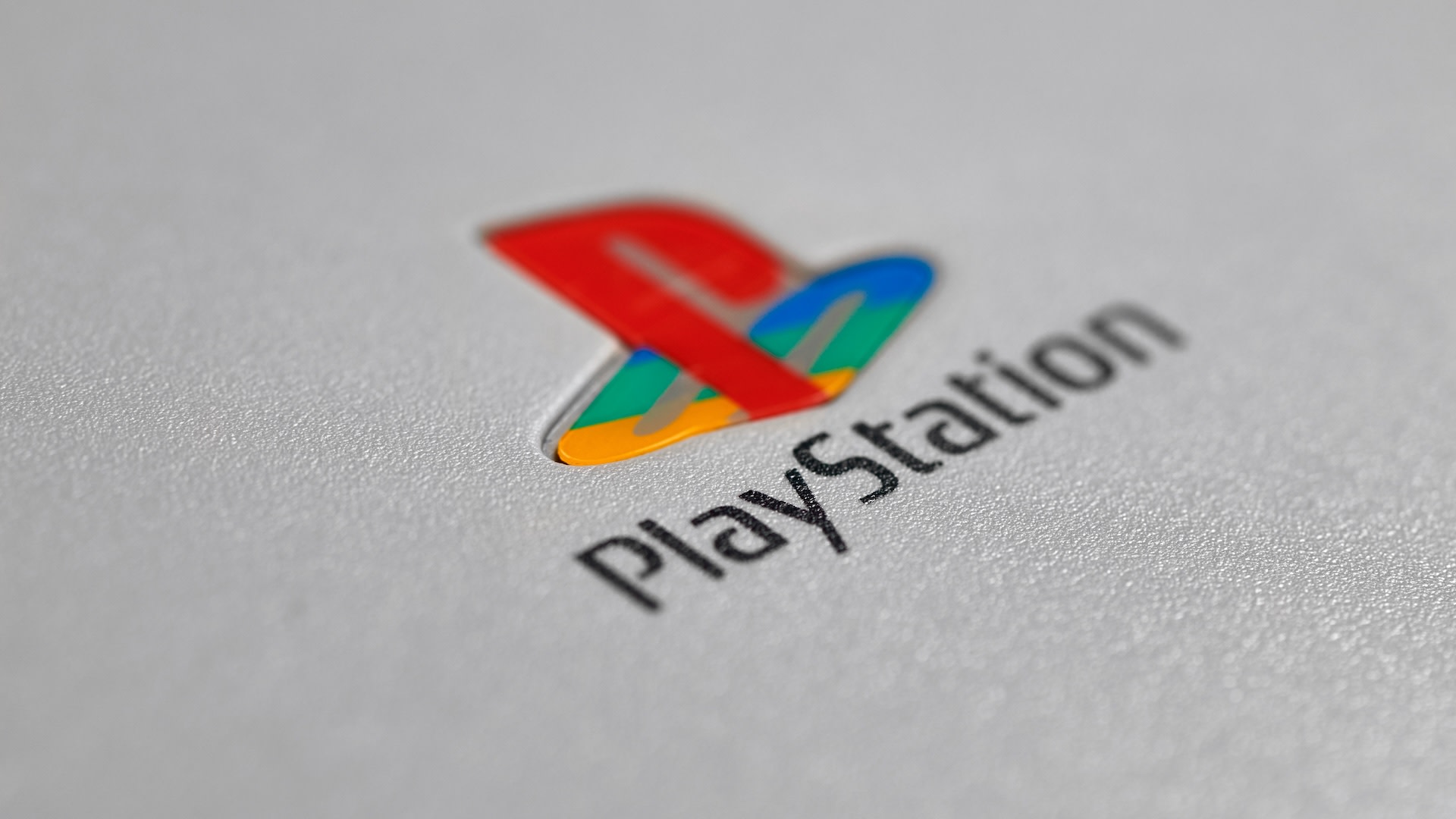 Close-up of the PlayStation logo on a gray surface, featuring a colorful "PS" symbol above the word "PlayStation."