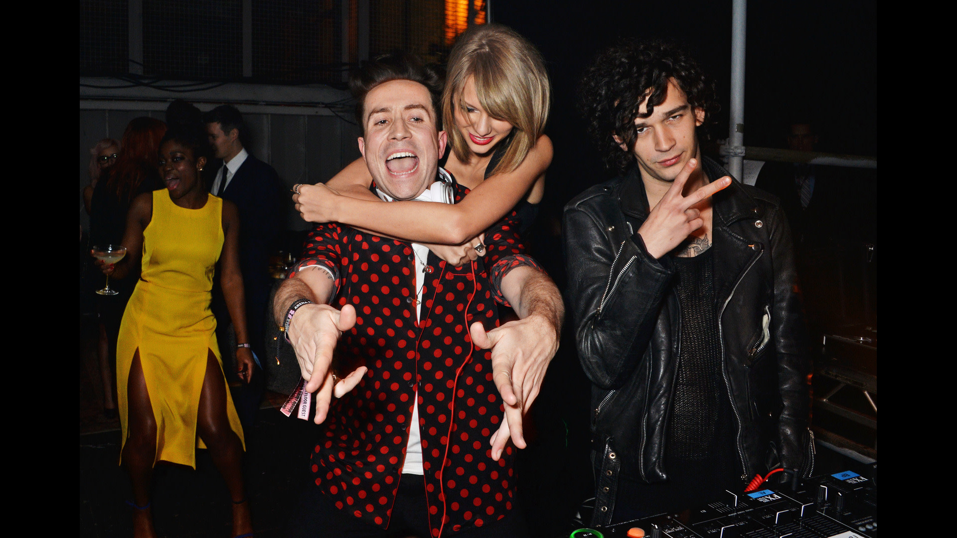 Nick Grimshaw in a red polka dot shirt, Taylor Swift hugging him, and Matty Healy in a leather jacket, posing at an event.