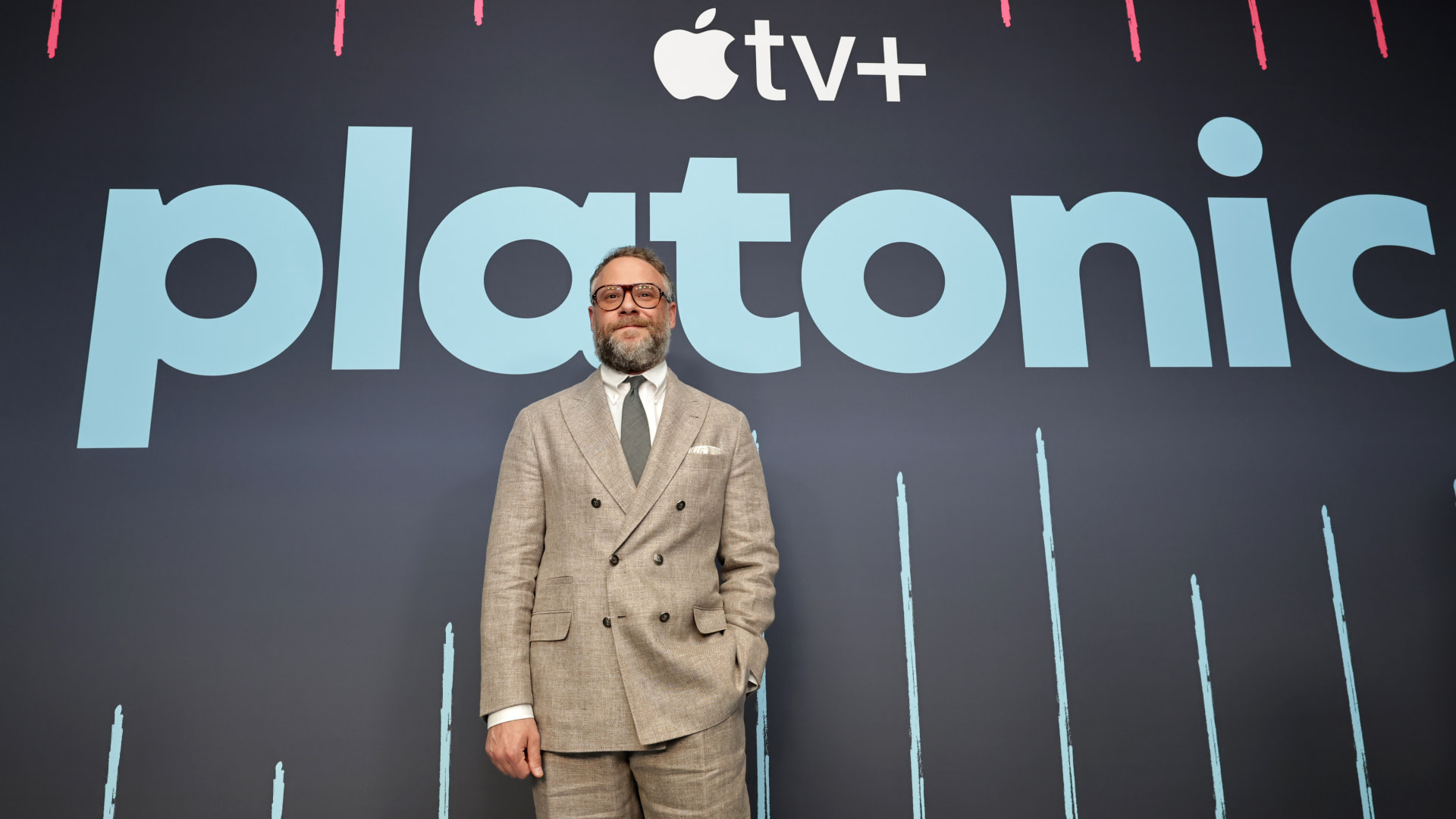 Seth Rogen in a suit stands in front of a backdrop with the Apple TV+ logo and the word "Platonic."