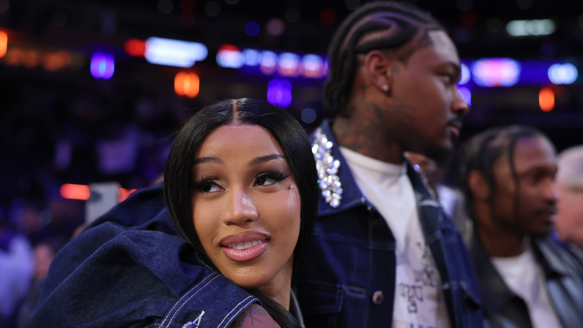 A woman with long black hair and a man with braided hair are at a sports event, both wearing denim jackets.