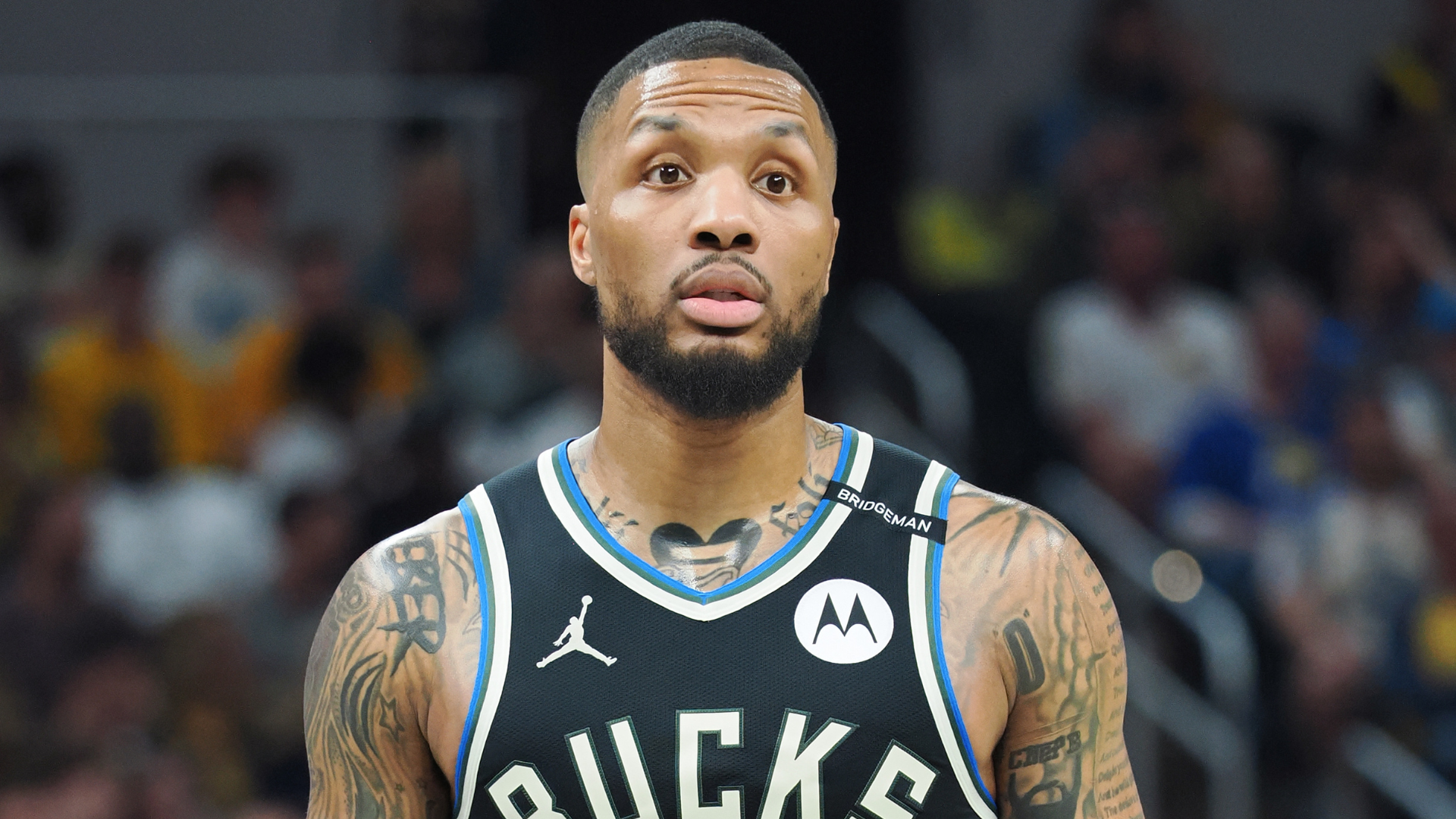 A basketball player wearing a Milwaukee Bucks jersey during a game, with tattoos on his arms and neck.