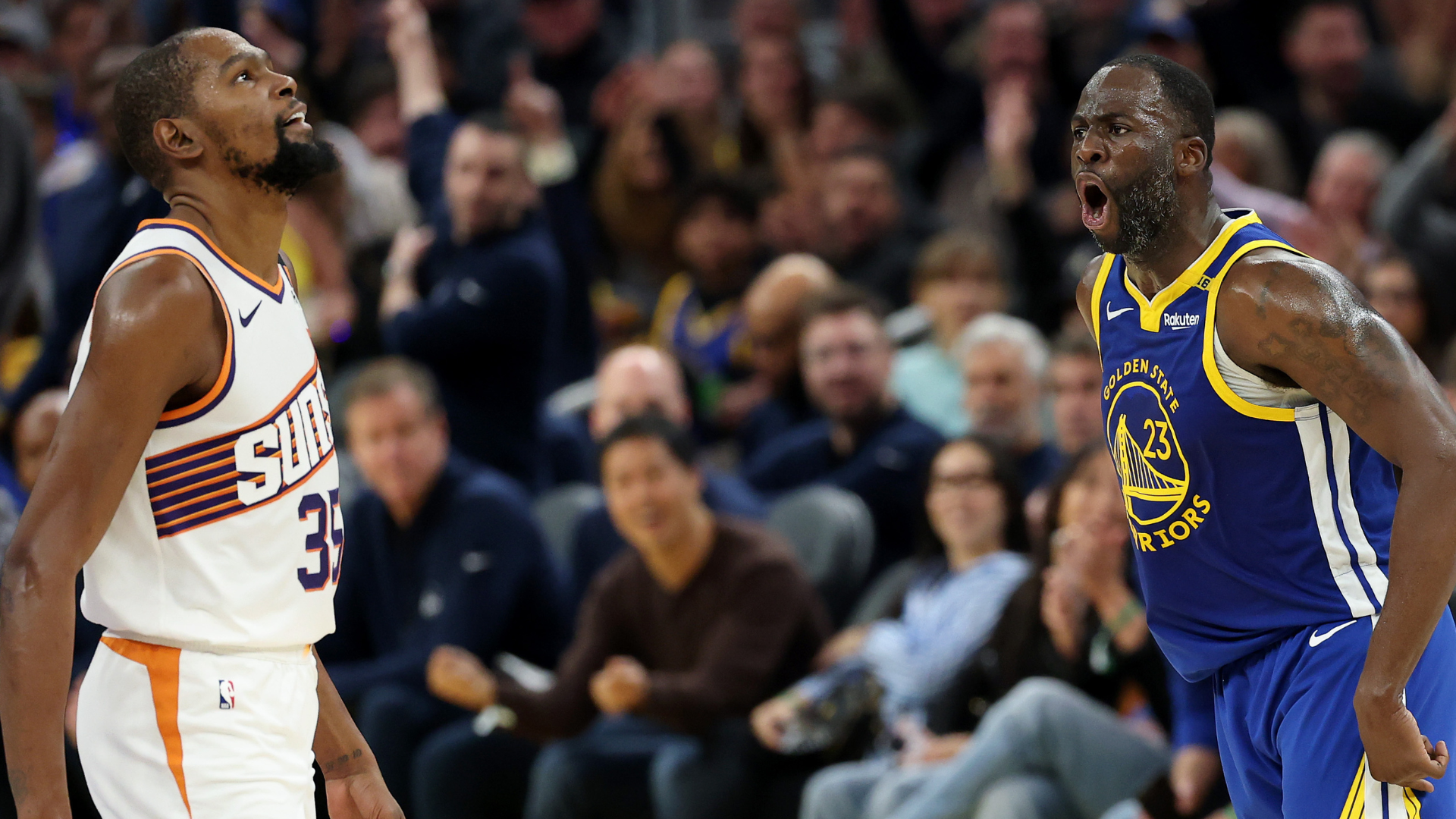 Kevin Durant in a Phoenix Suns jersey and Draymond Green in a Golden State Warriors jersey during an intense moment on court.