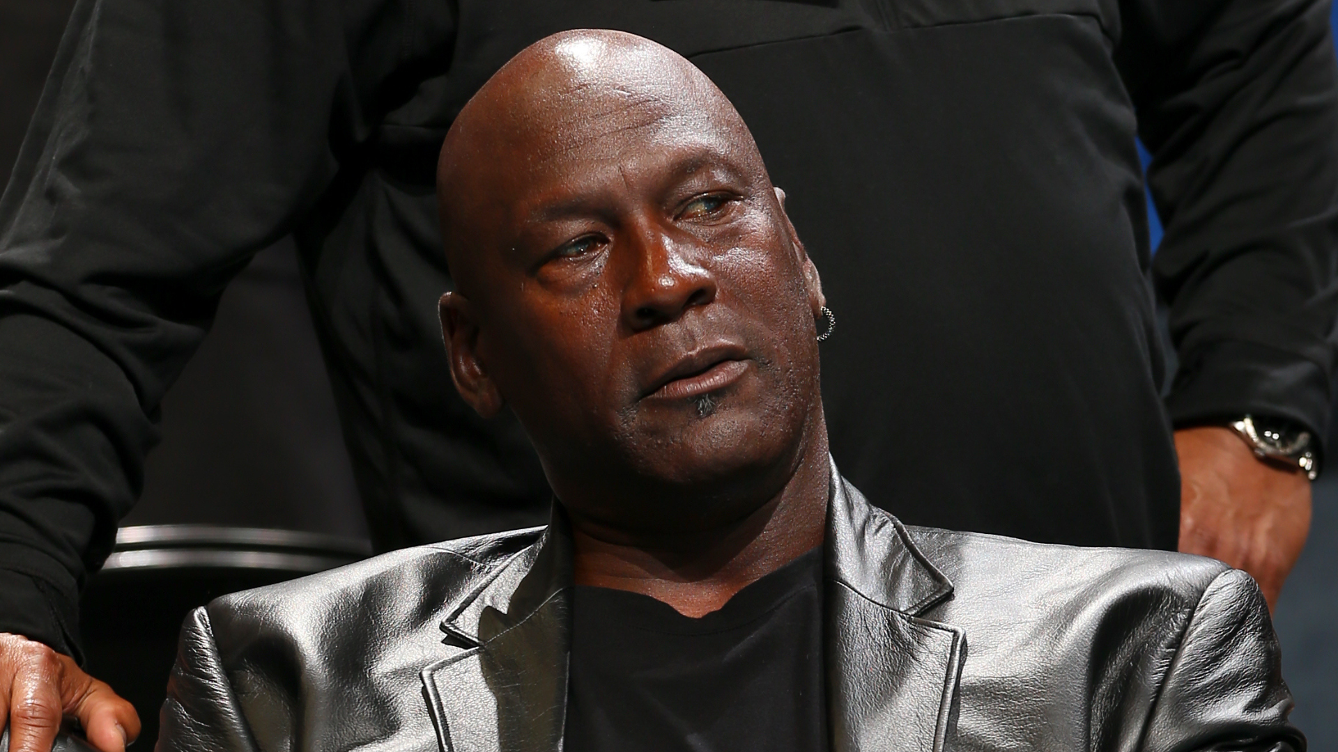 A man in a shiny black jacket looking to the side, with a contemplative expression.