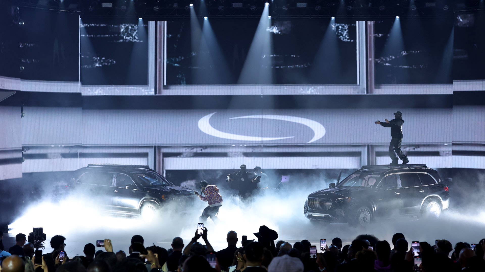 A Playboi Carti stage performance with two SUVs, fog effects, dancers, and an audience capturing the scene.