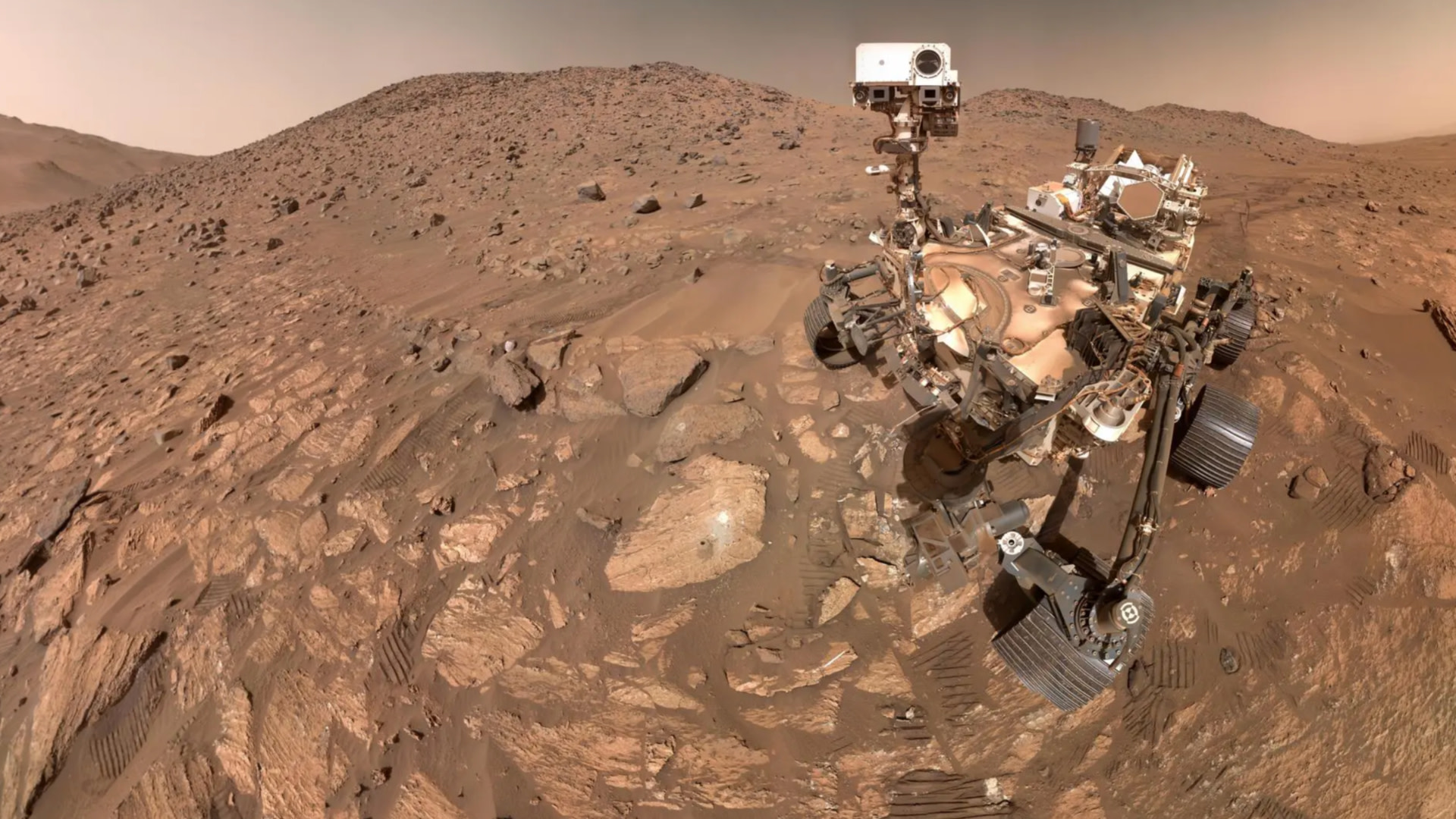 NASA's Perseverance rover on Mars, capturing a selfie on a rocky, dusty Martian landscape with hills in the background.