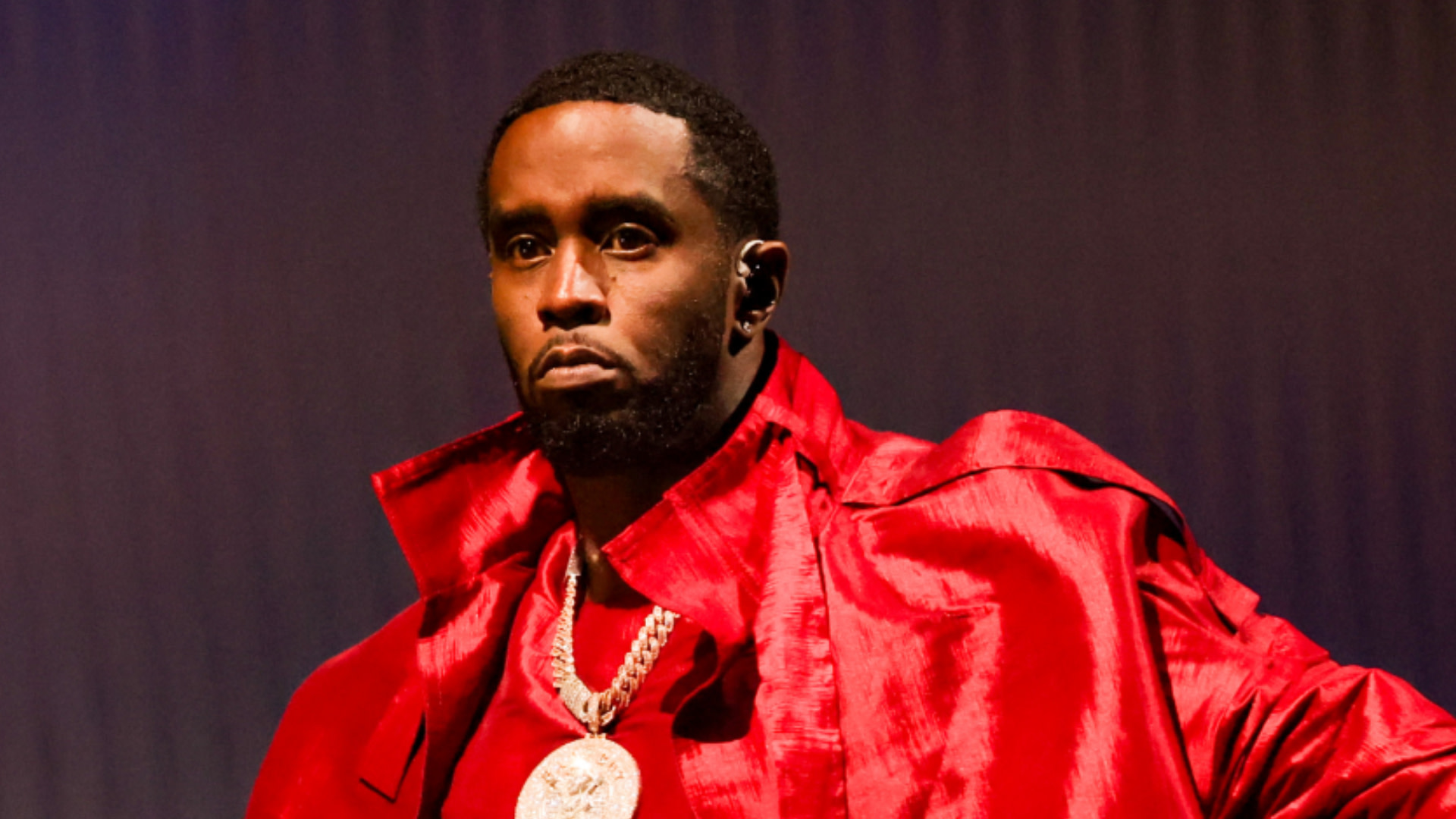 Sean "Diddy" Combs wearing a red outfit and large chain, looking serious.