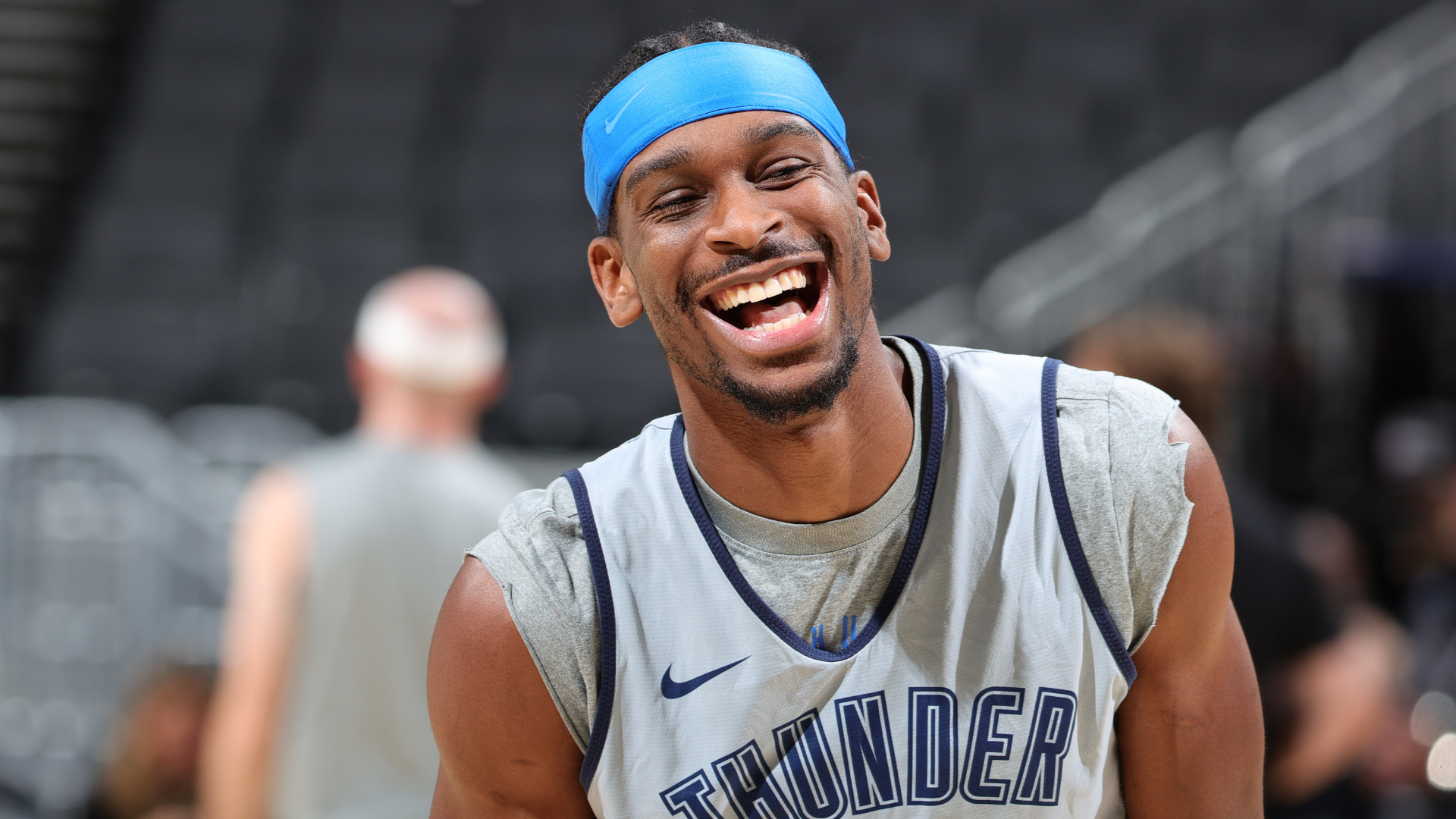 A basketball player wearing a "Thunder" jersey and a blue headband is smiling widely on the court.