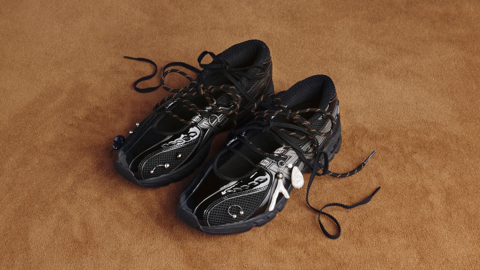 A pair of black and white sneakers with intricate designs and black laces, placed on a brown surface.