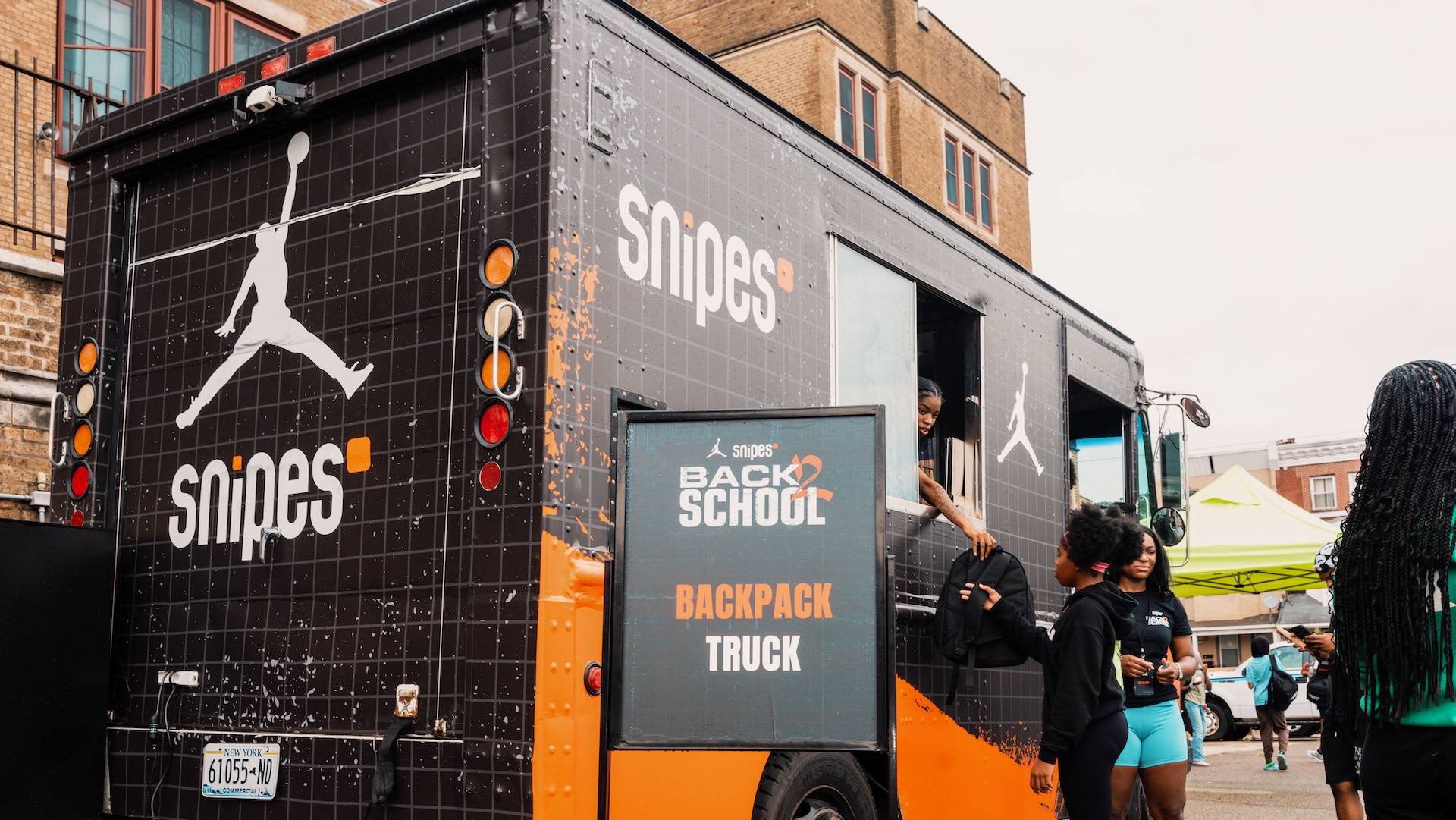 A Snipes "Back to School" backpack truck with a Jordan logo, parked outdoors. People are interacting with the truck.