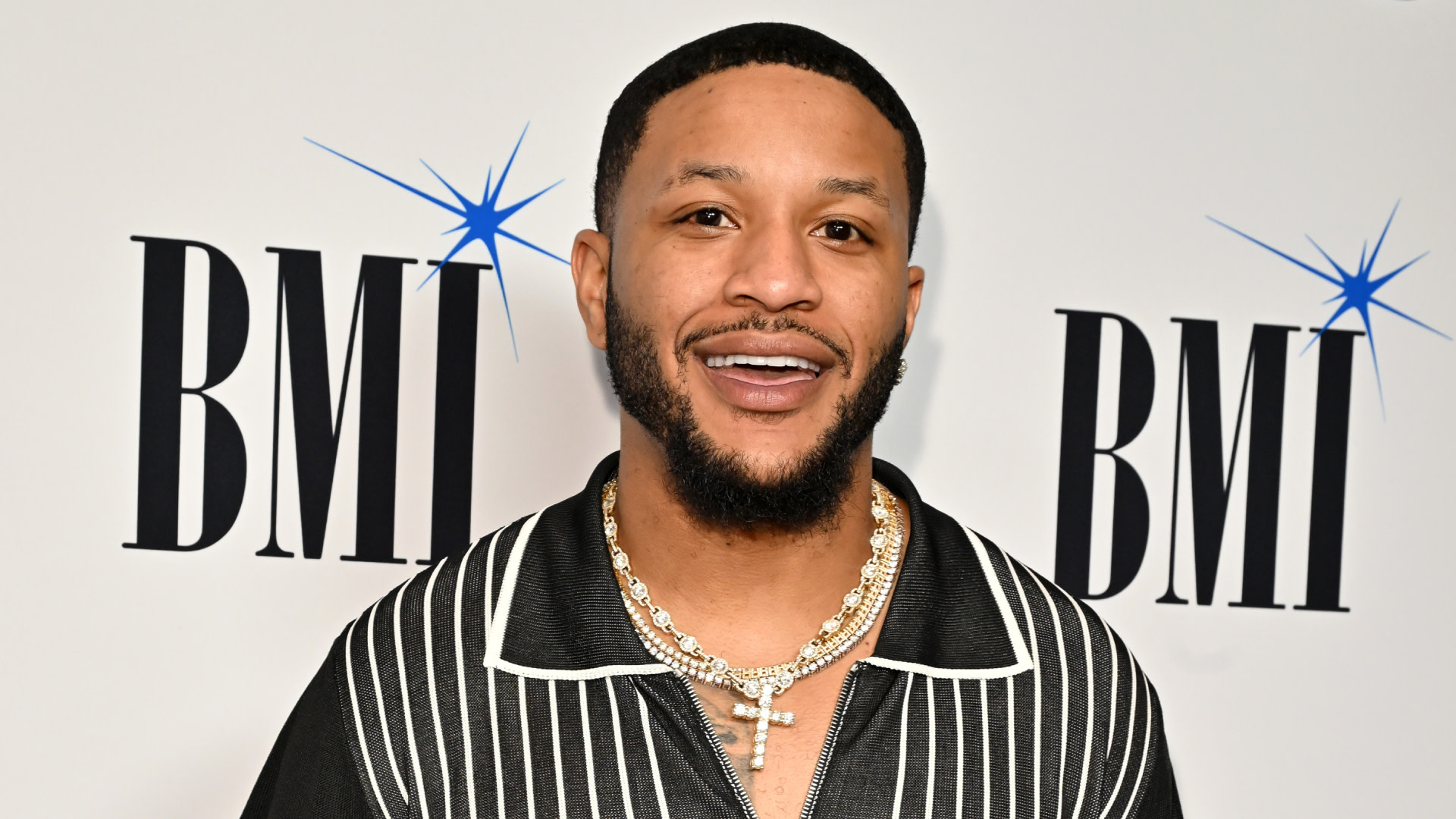 BenDaDonnn smiles at a BMI event, wearing a black and white striped shirt and a gold chain necklace.