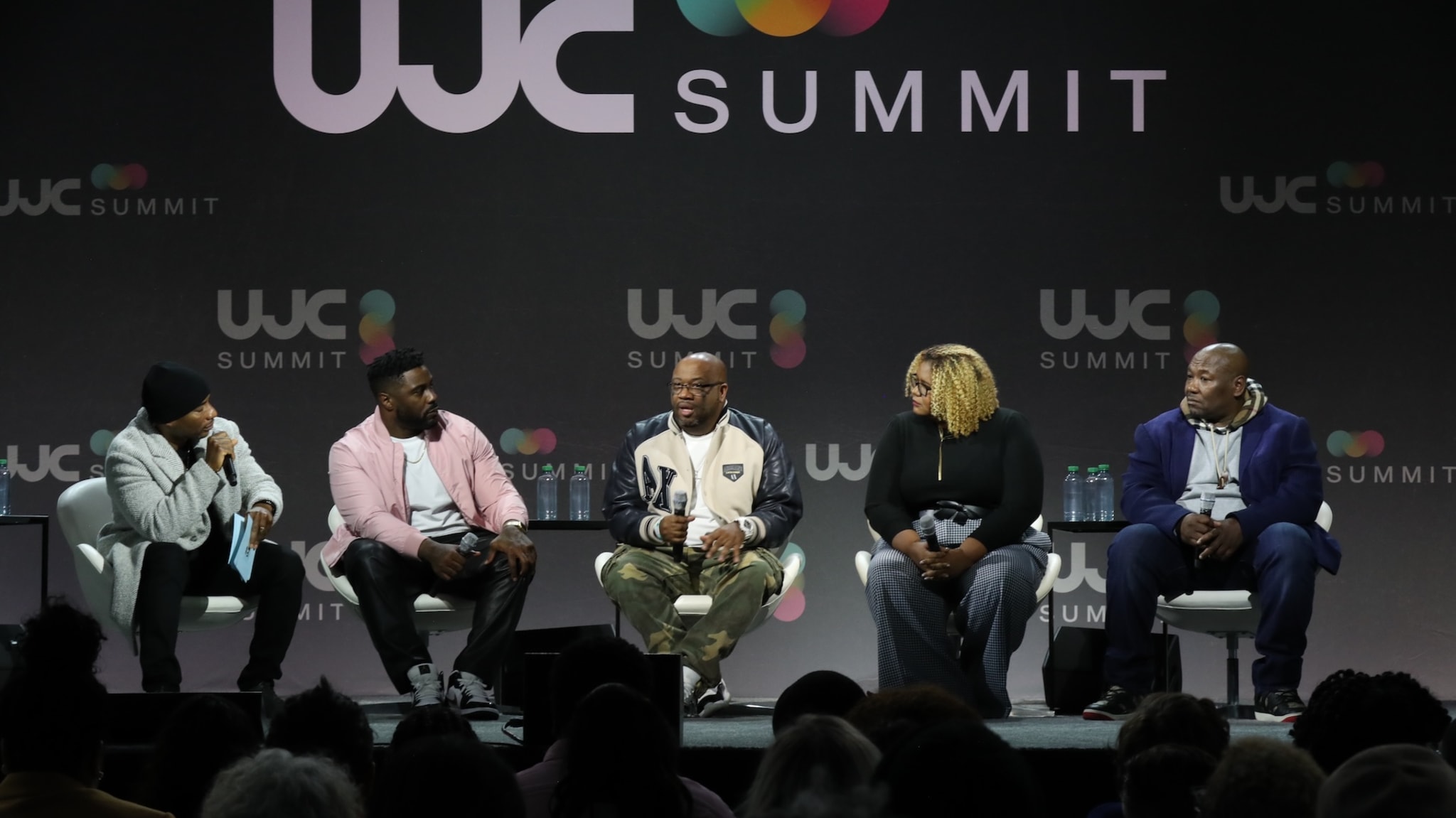 A panel of five people seated on stage at the WJC Summit, engaging in discussion.