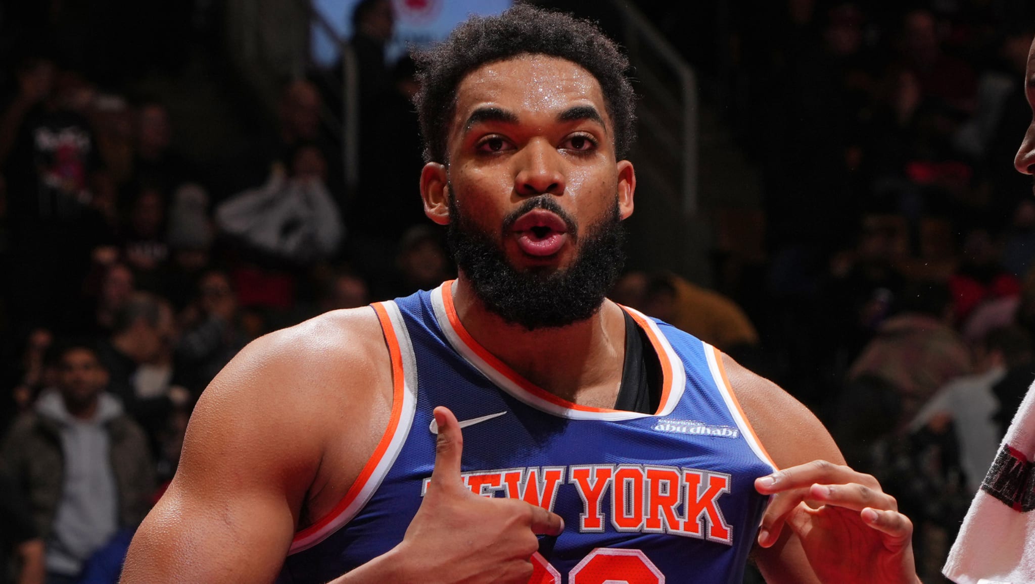 Basketball player in a New York jersey on the court, gesturing with his hands, with a crowd in the background.