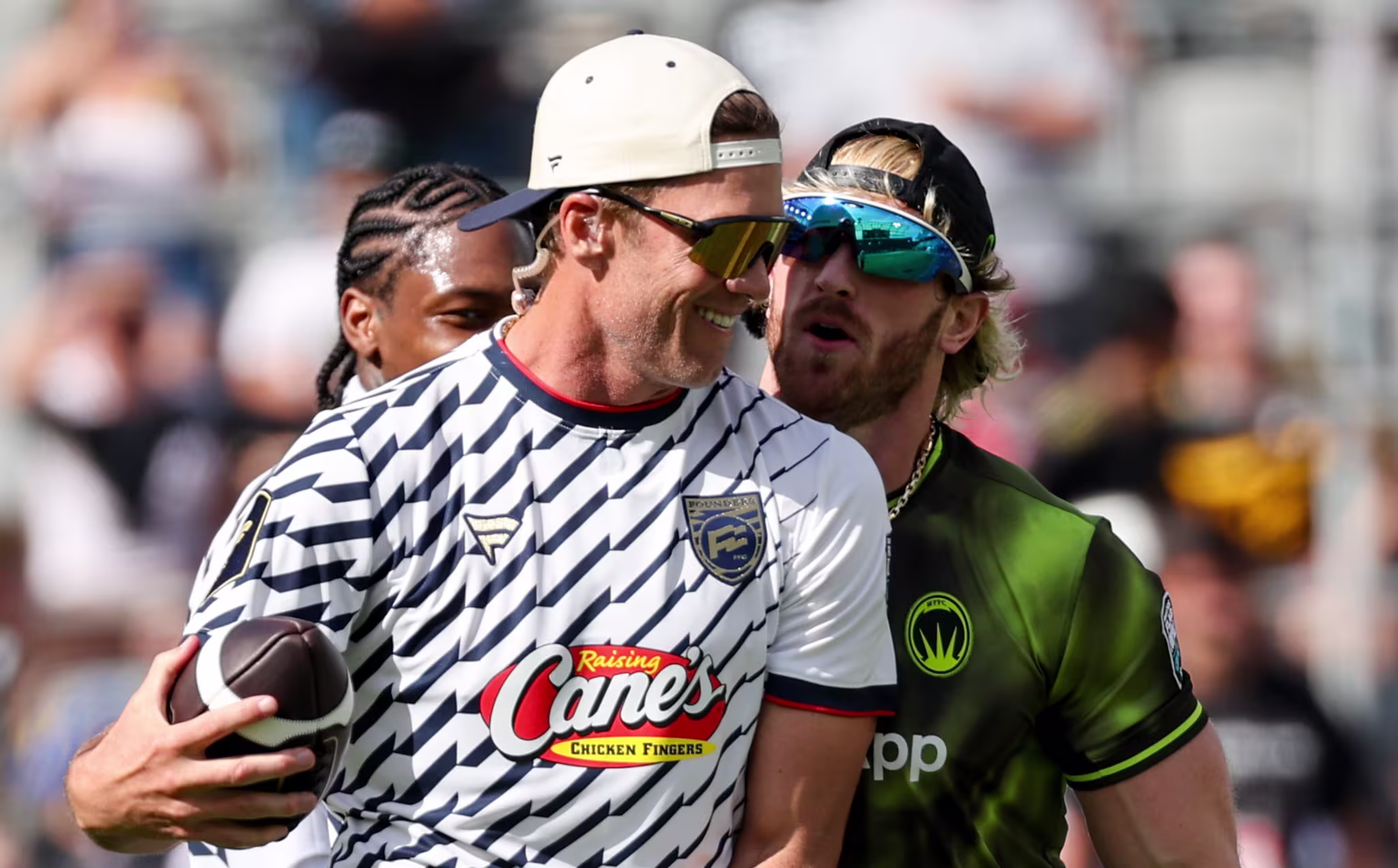 Tom Brady holding a football and wearing a cap, Logan Paul in sunglasses and a green jersey.