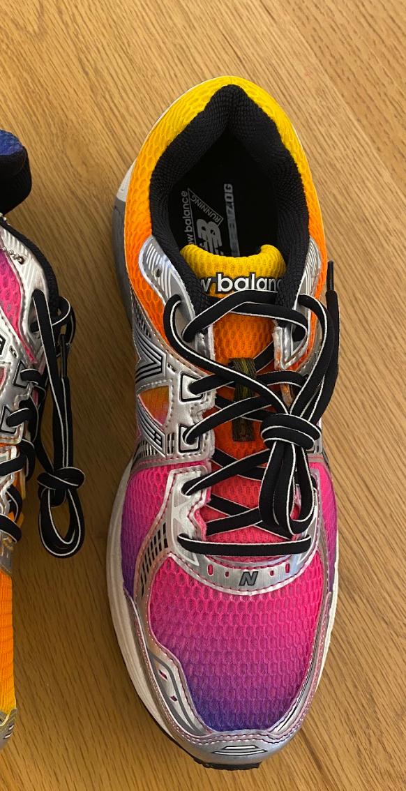 Colorful New Balance sneakers on a wooden floor, featuring a gradient of orange, purple, and pink with a tag labeled "1 of 150."