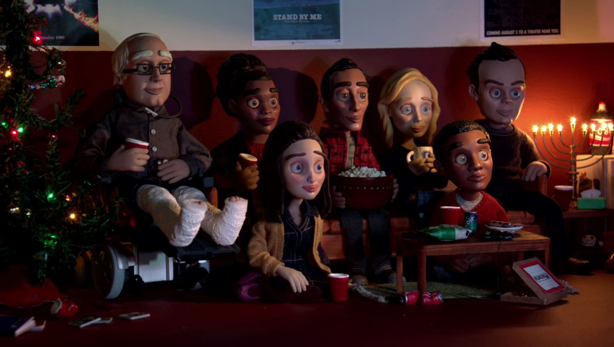 Claymation figures resembling the cast of 'Community' sitting on a couch, celebrating Christmas and Hanukkah with decorations around.