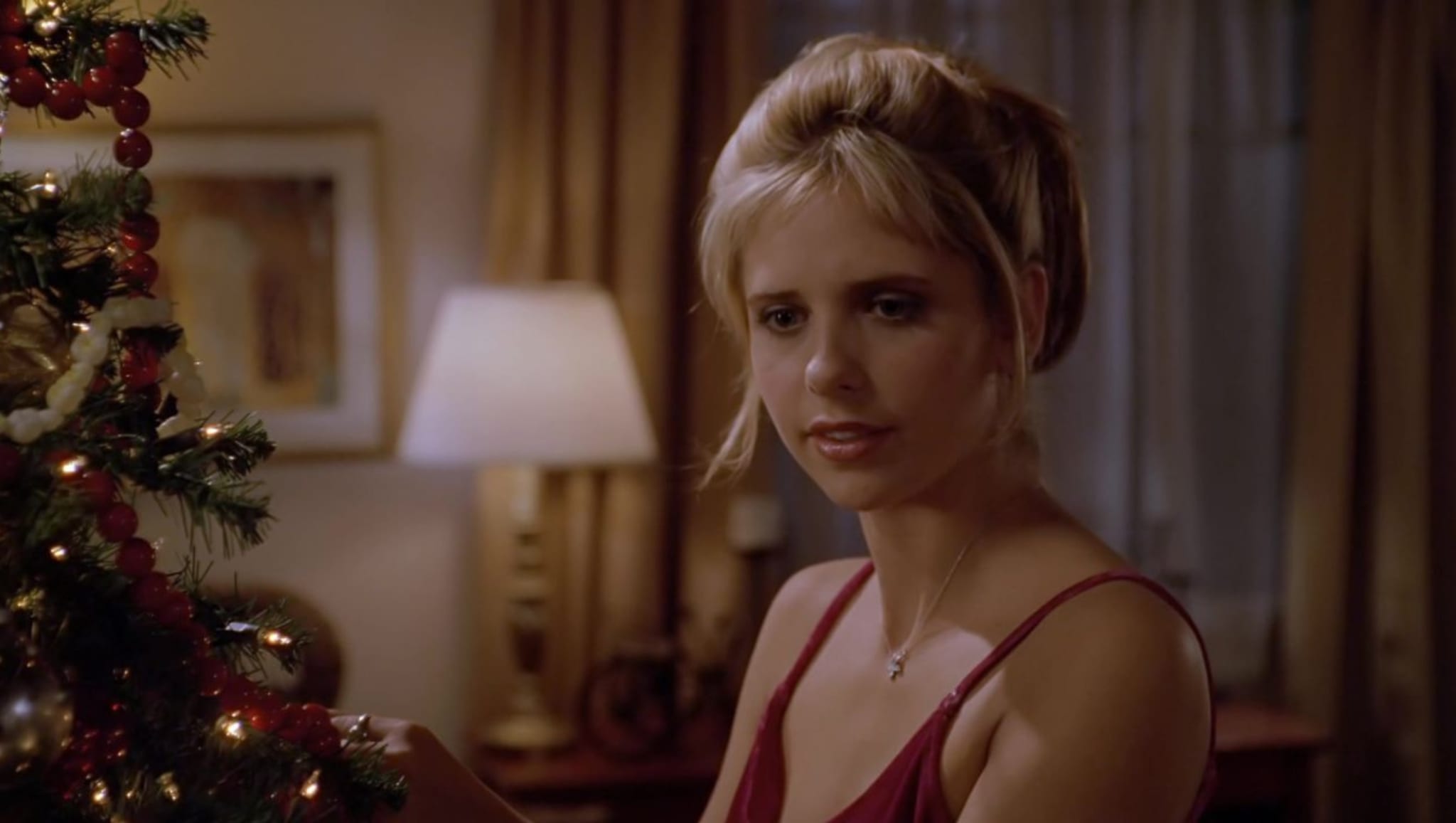 A woman in a red dress decorates a Christmas tree in a warmly lit room.