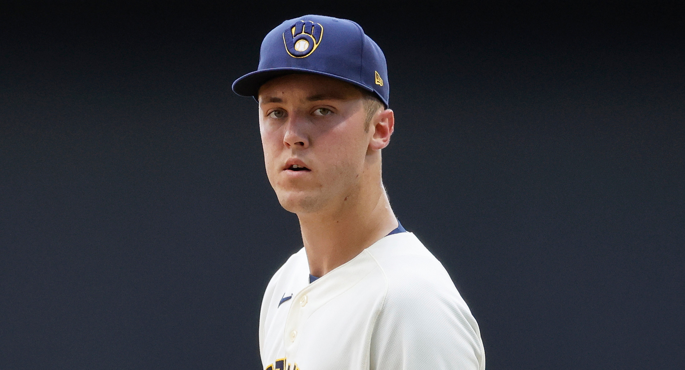 Jacob Misiorowski, in a Milwaukee Brewers uniform, stands on the field holding a baseball and a glove, looking towards the camera.