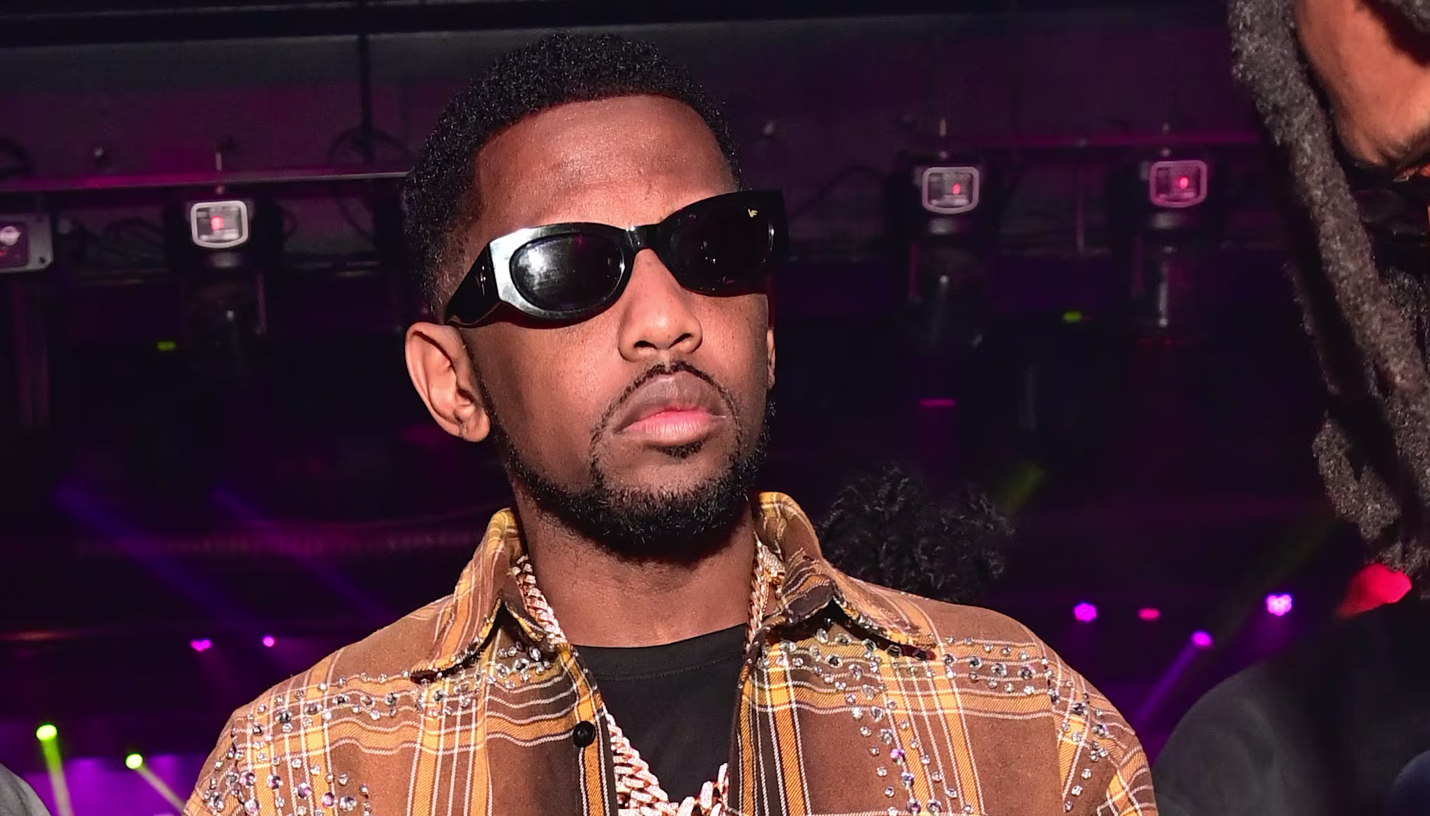 Fabolous in a nightclub, wearing a stylish outfit and jewelry.