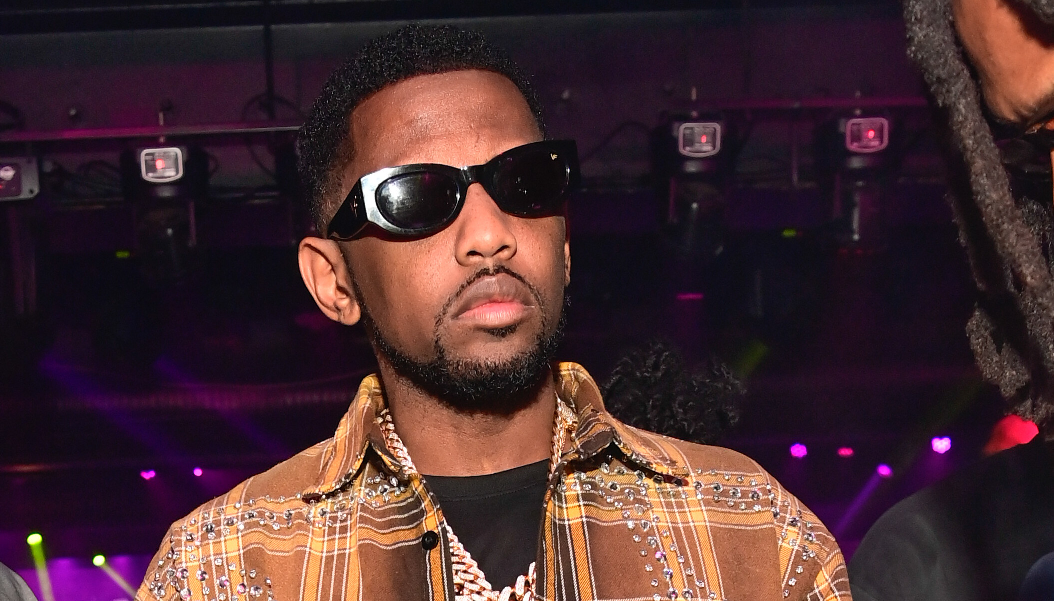 Fabolous in a nightclub, wearing a stylish outfit and jewelry.