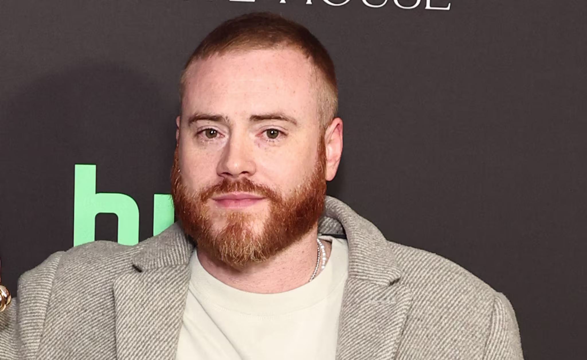 Rory Farrell in a gray coat pose on a red carpet. They stand against a backdrop with logos.