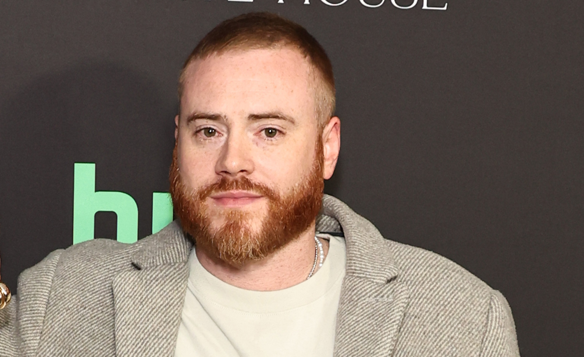 Rory Farrell in a gray coat pose on a red carpet. They stand against a backdrop with logos.