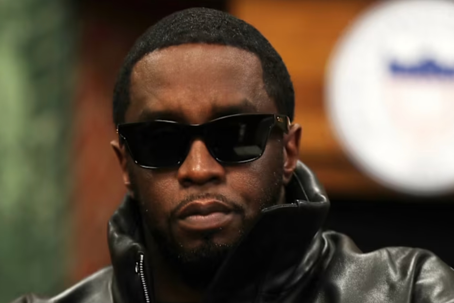 Diddy wearing sunglasses and a leather jacket, looking serious.
