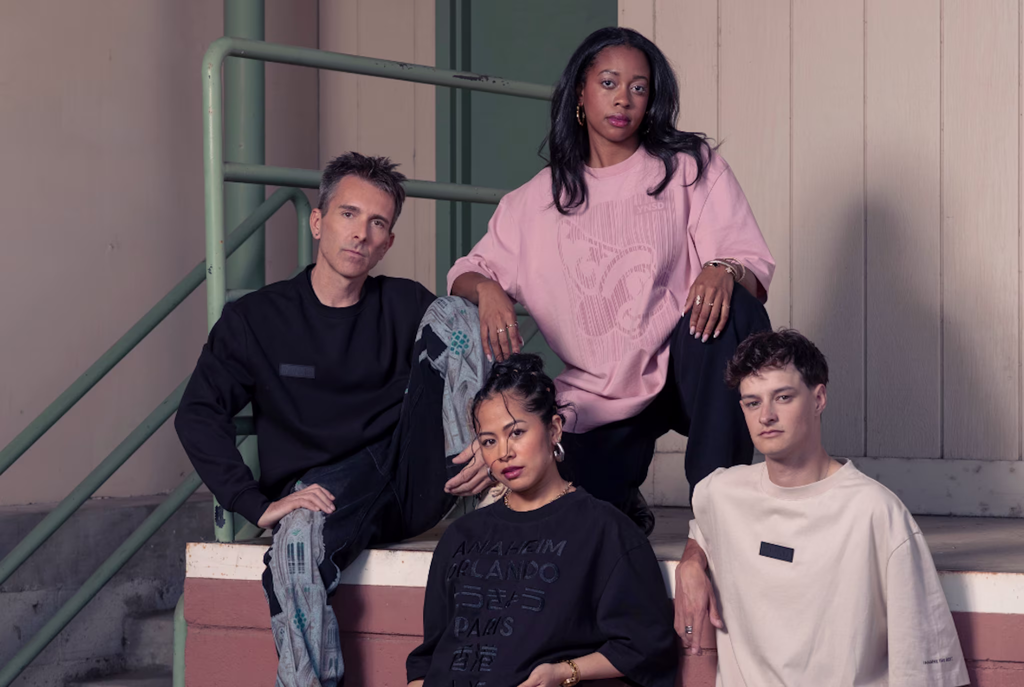 A group of four people posing fashionably on stairs, wearing casual and stylish clothing in neutral tones.