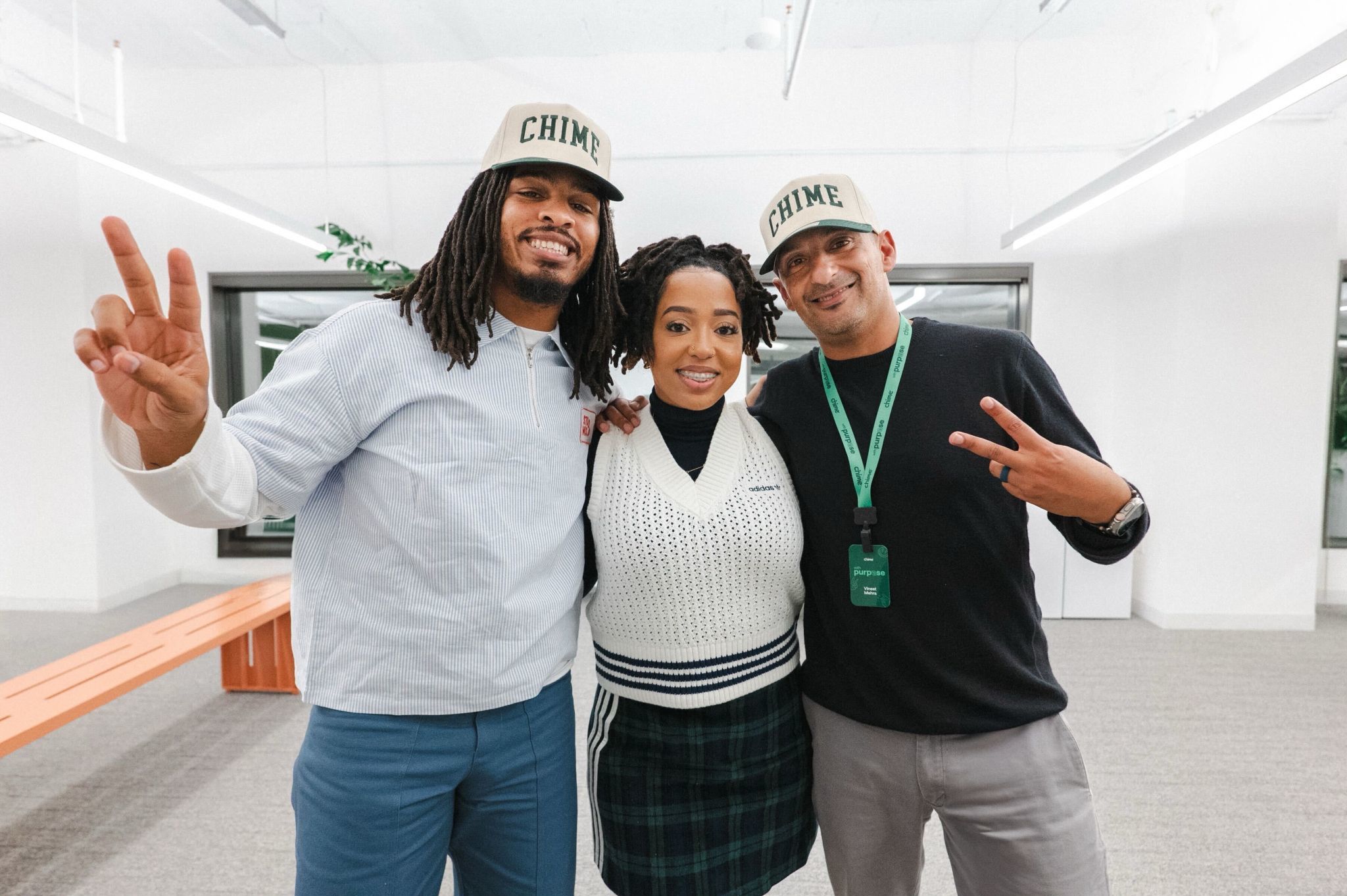 Three people pose together indoors, two wearing "Chime" hats. They smile and make peace signs in a modern office setting.