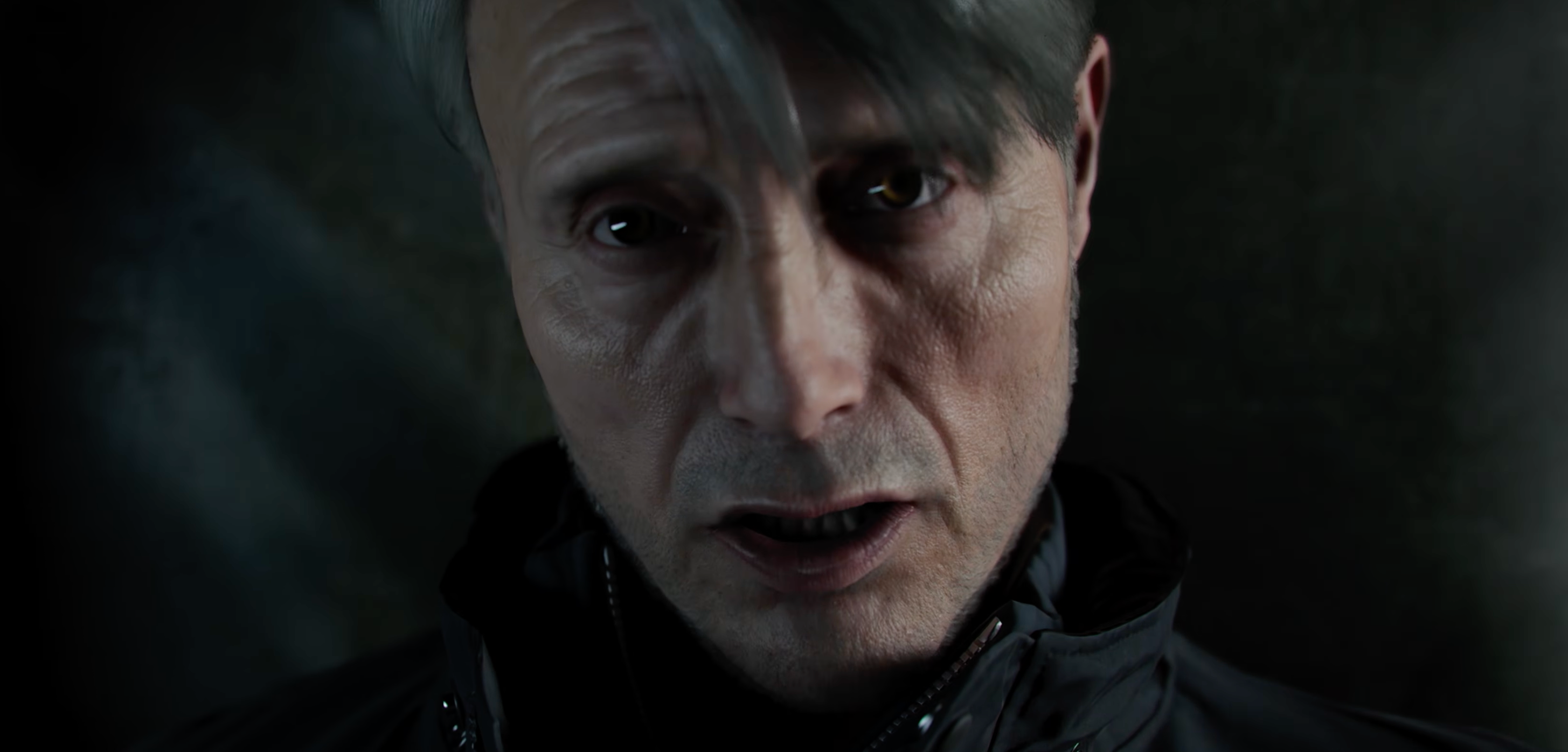 A close-up of a man with gray hair and a serious expression, wearing a dark jacket, looking directly at the camera.