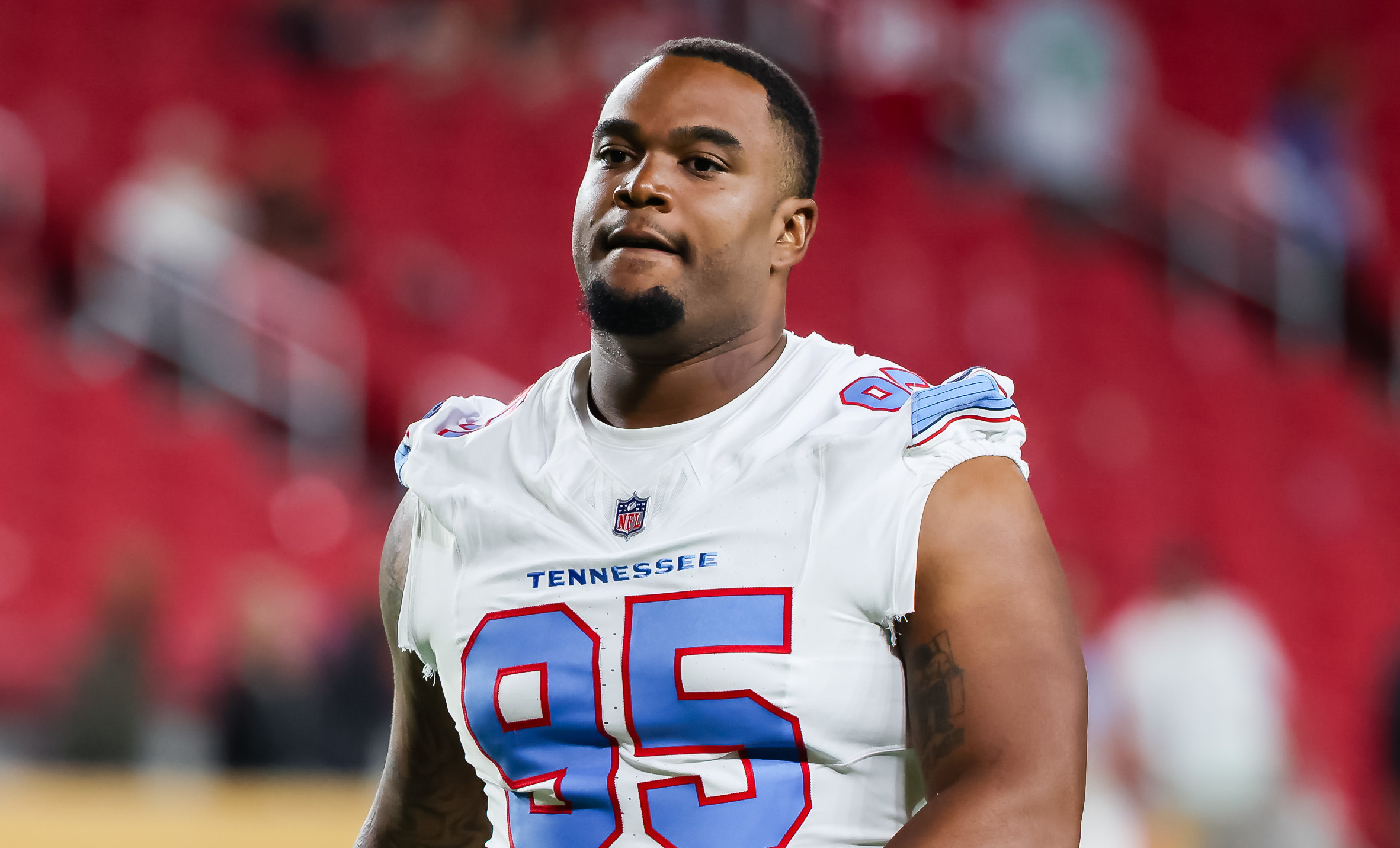 Jordan Elliott in a Tennessee Titans jersey, number 95, on the field with a red stadium background.