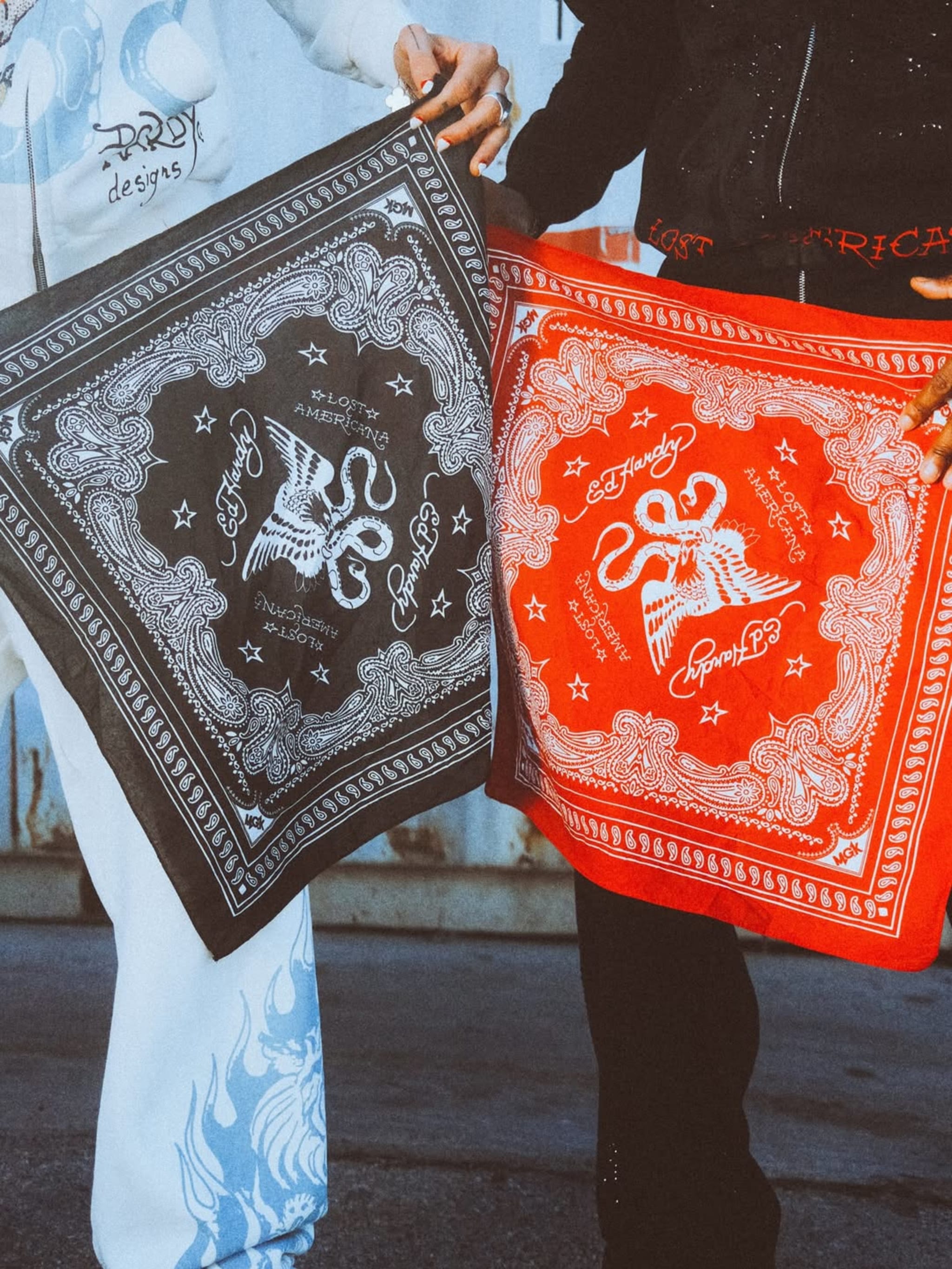 Two people holding Ed Hardy bandanas, one black and one red, with intricate designs and text.