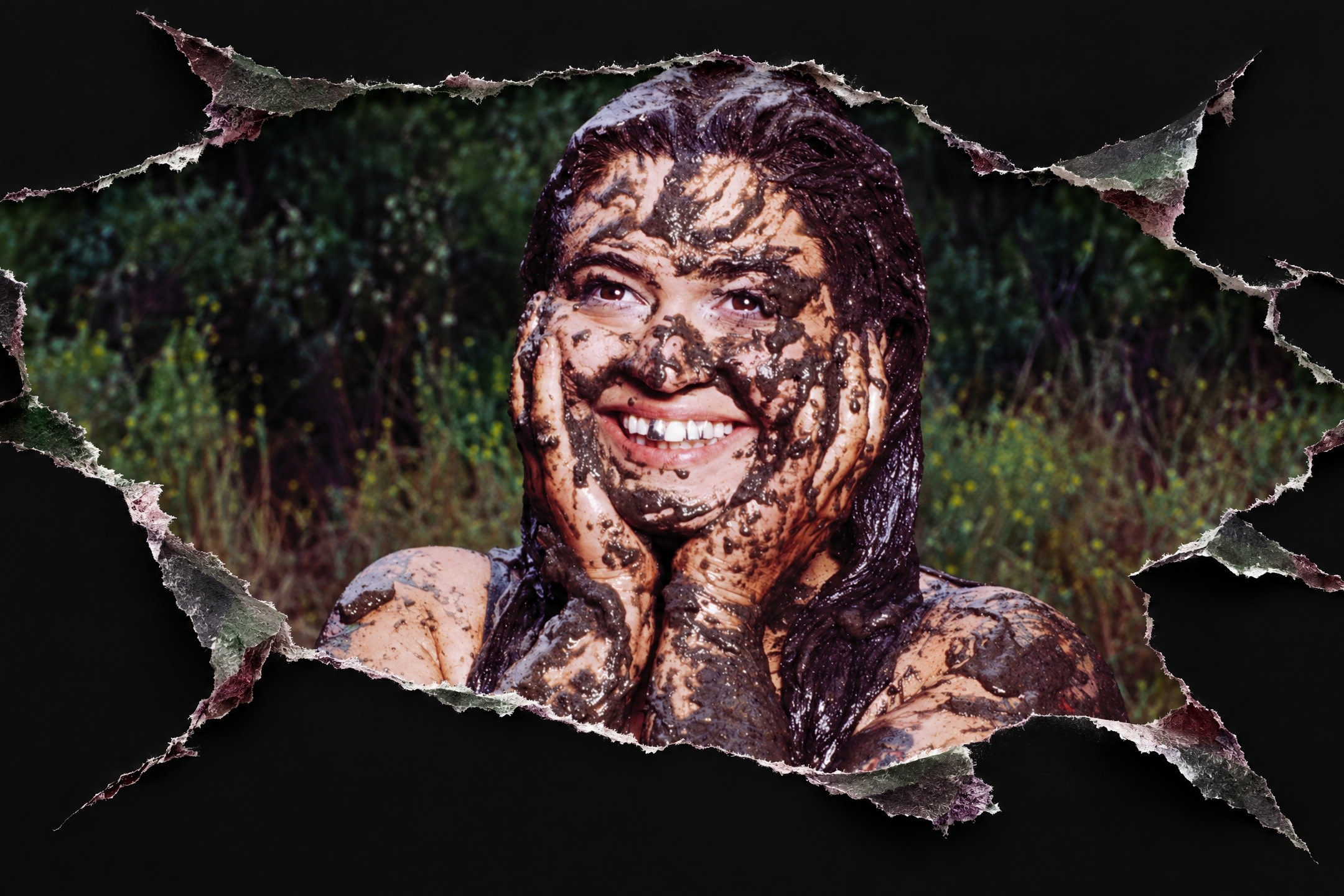 A person smiling, covered in mud, with hands on cheeks. The background shows greenery, framed by a torn paper effect.
