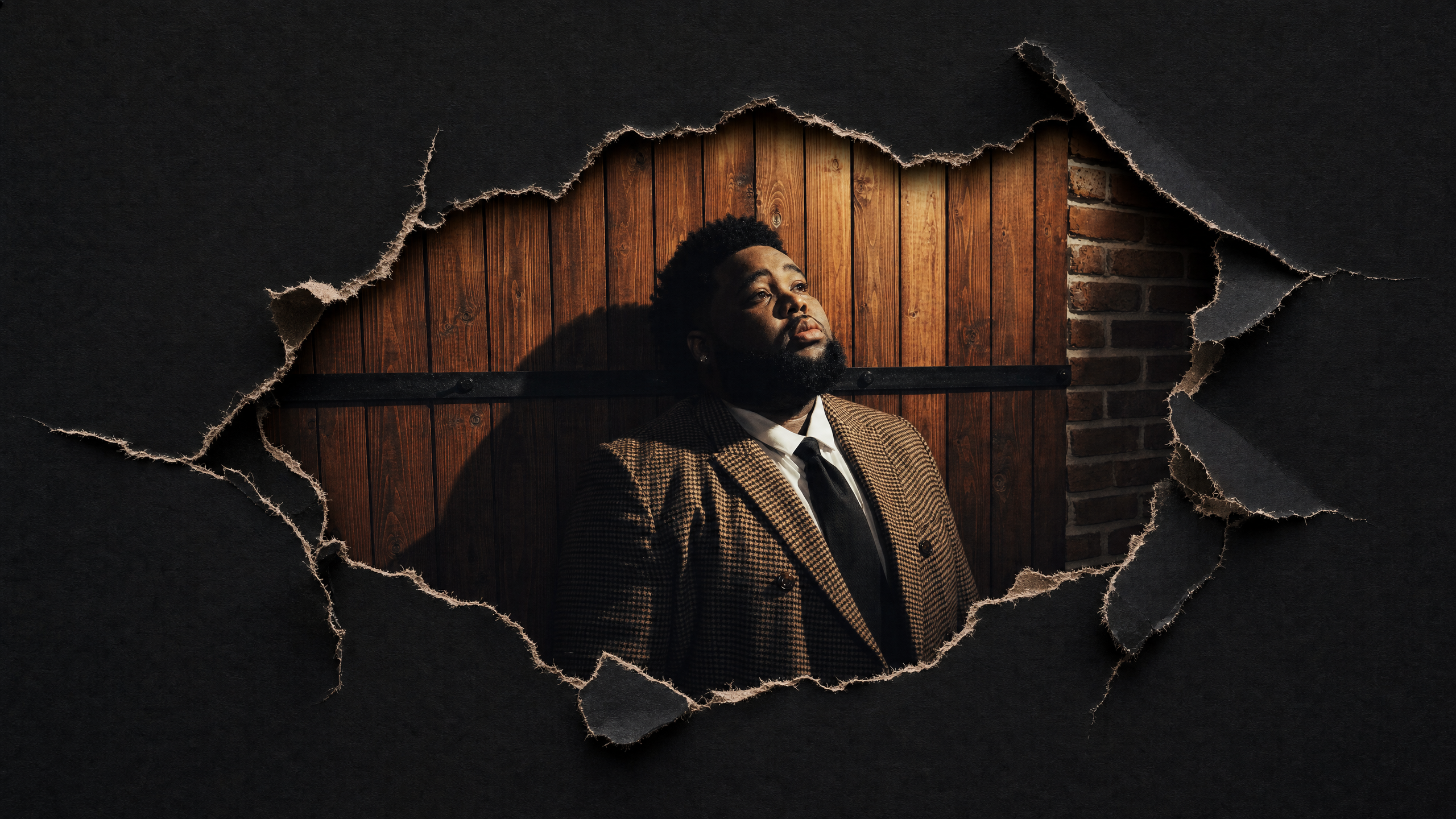 A man in a checkered suit and tie stands against a wooden backdrop, framed by a torn paper effect, gazing upwards.