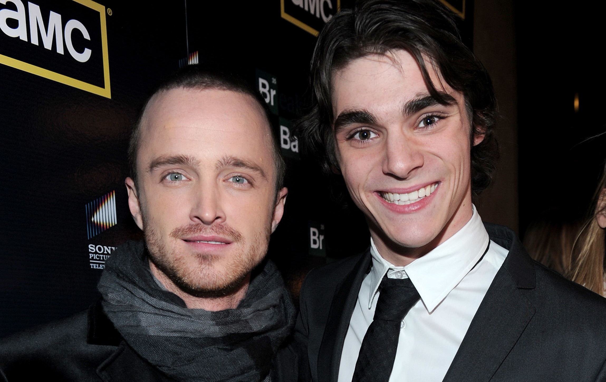 Aaron Paul and RJ Mitte at an AMC event, both in suits, smiling for the camera.