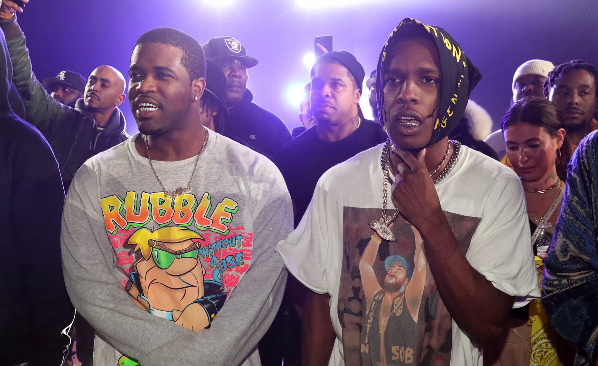 A$AP Ferg and A$AP Rocky at an event, surrounded by people, with bright lights in the background.