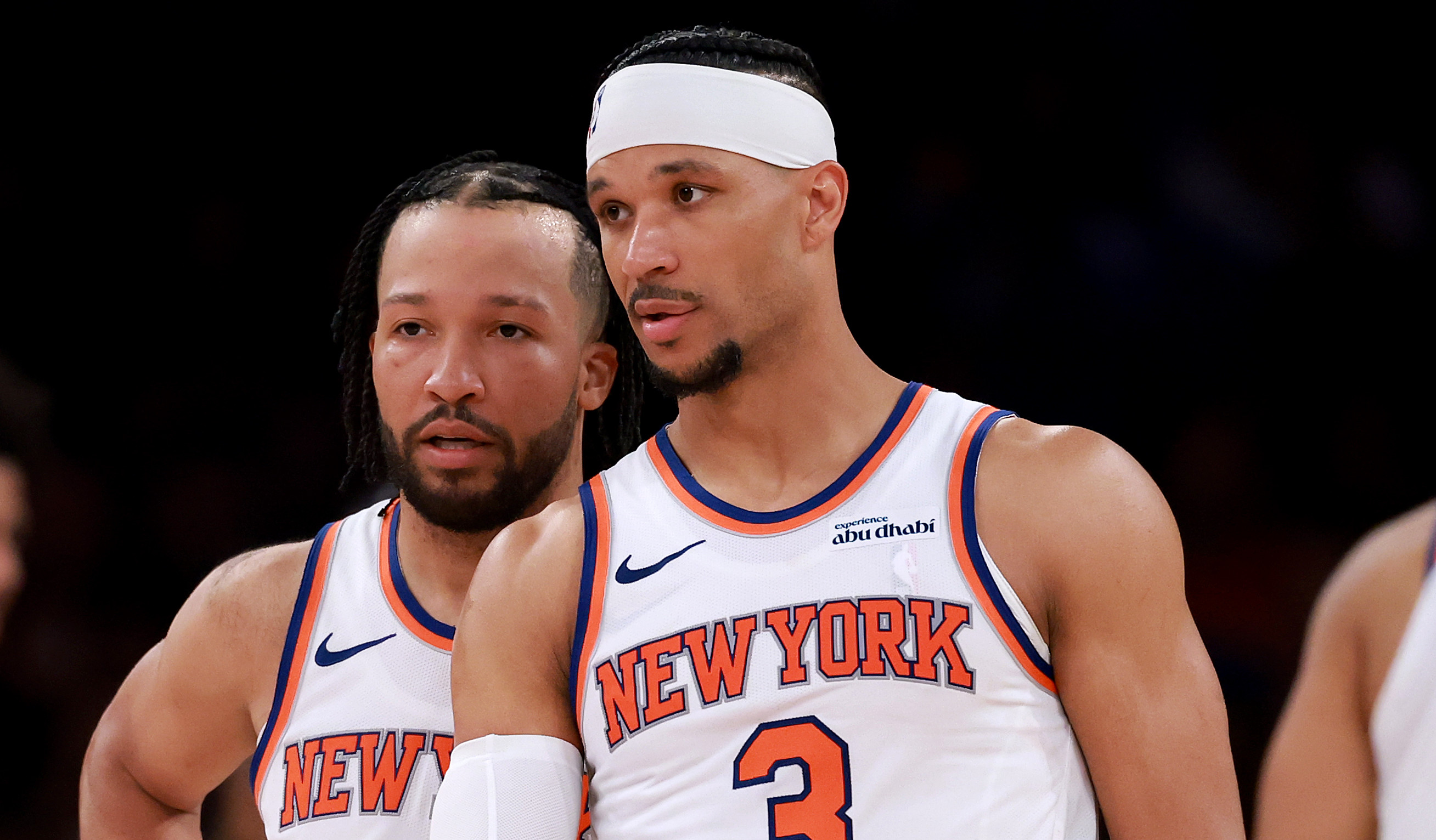 Jalen Brunson and Josh Hart in white jerseys during a game, one wearing a headband and arm sleeve.