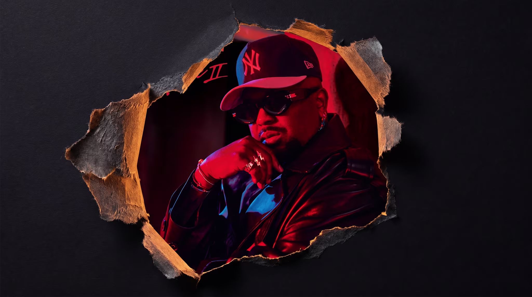A person in a leather jacket and sunglasses, wearing a New York Yankees cap, seen through a torn paper effect with red lighting.