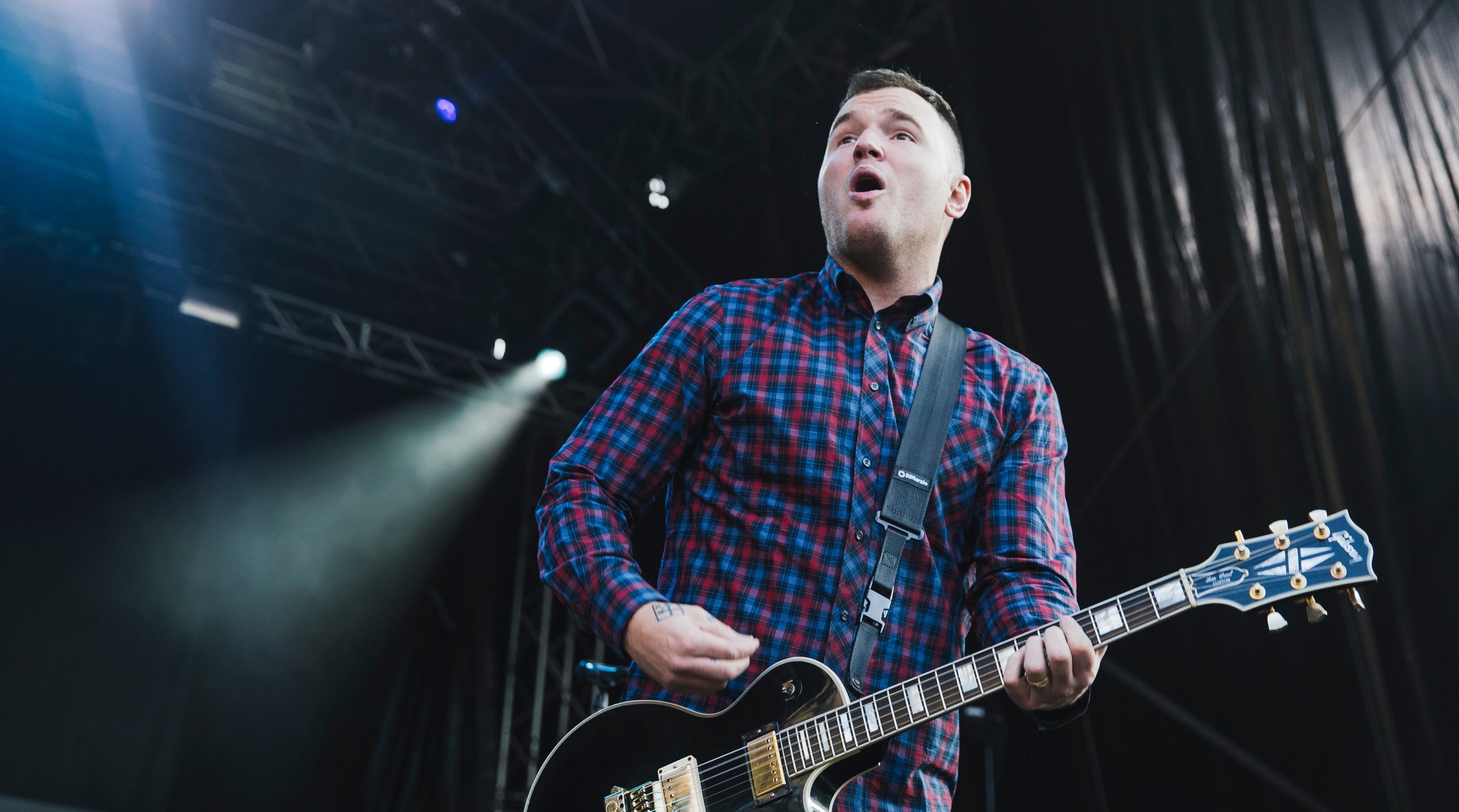 Chad Gilbert performing energetically on stage with a colorful background and a band member in the background.