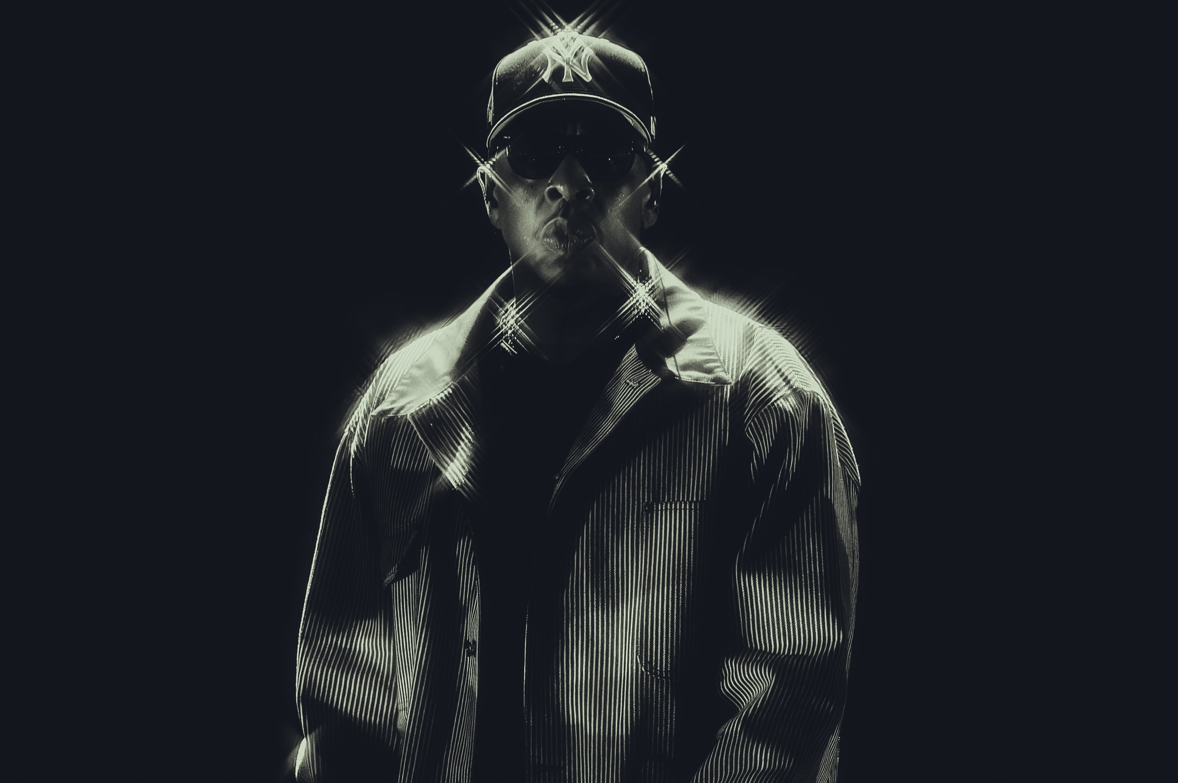 A person in a New York Yankees cap and jacket stands against a dark background, with light reflecting off them dramatically.