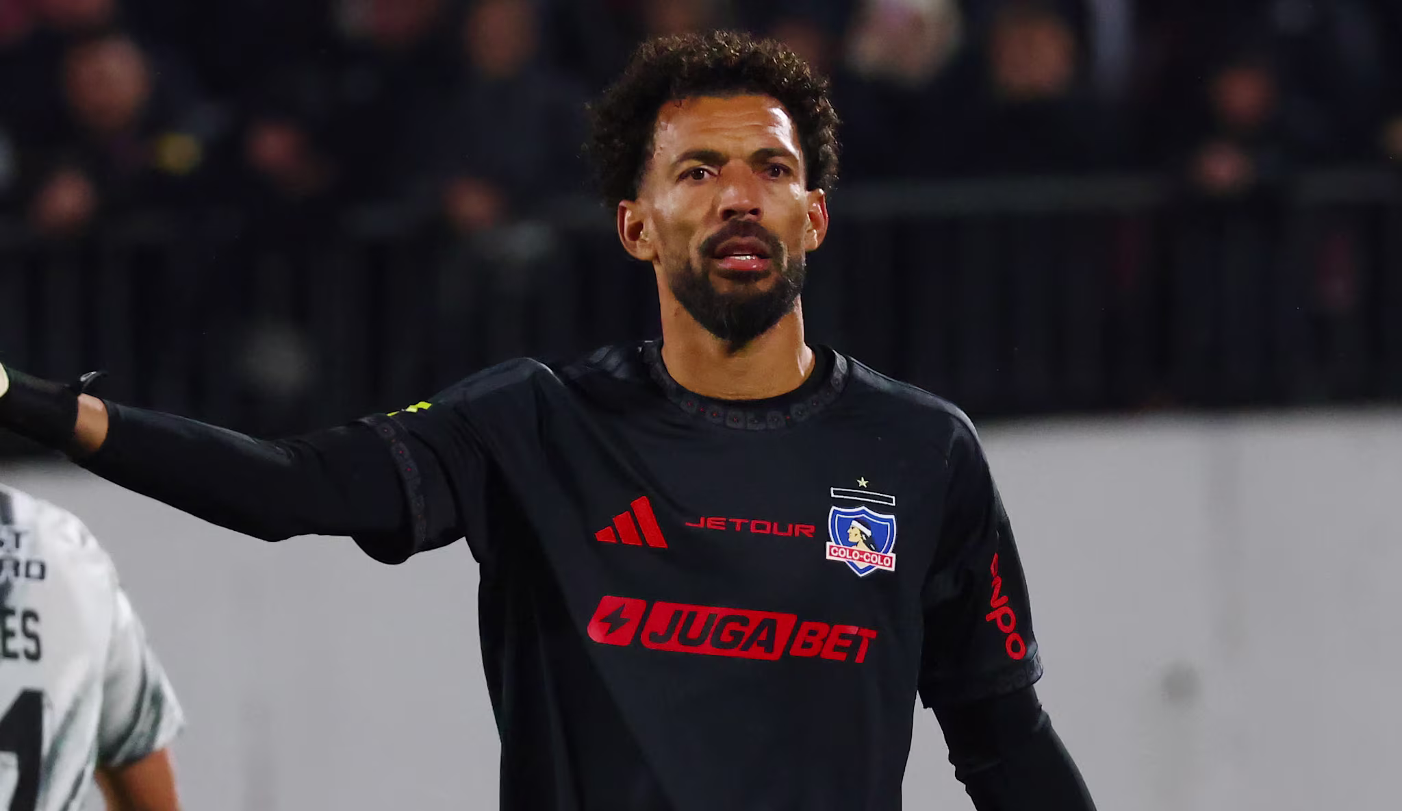 Vozinha in a black goalkeeper uniform gestures on the field, with another player wearing a white jersey in the background.