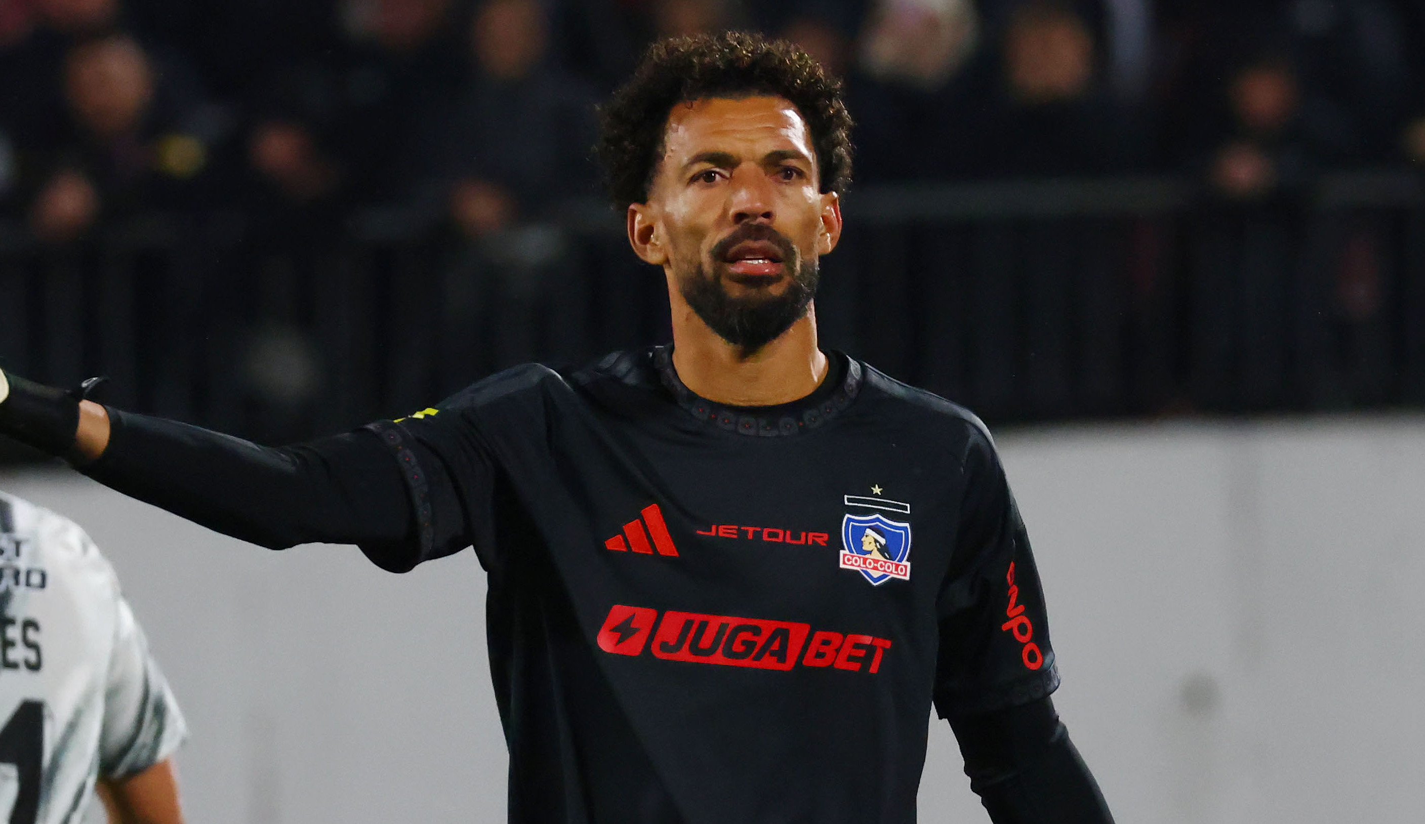 Vozinha in a black goalkeeper uniform gestures during a match, with another player in a white jersey in the background.