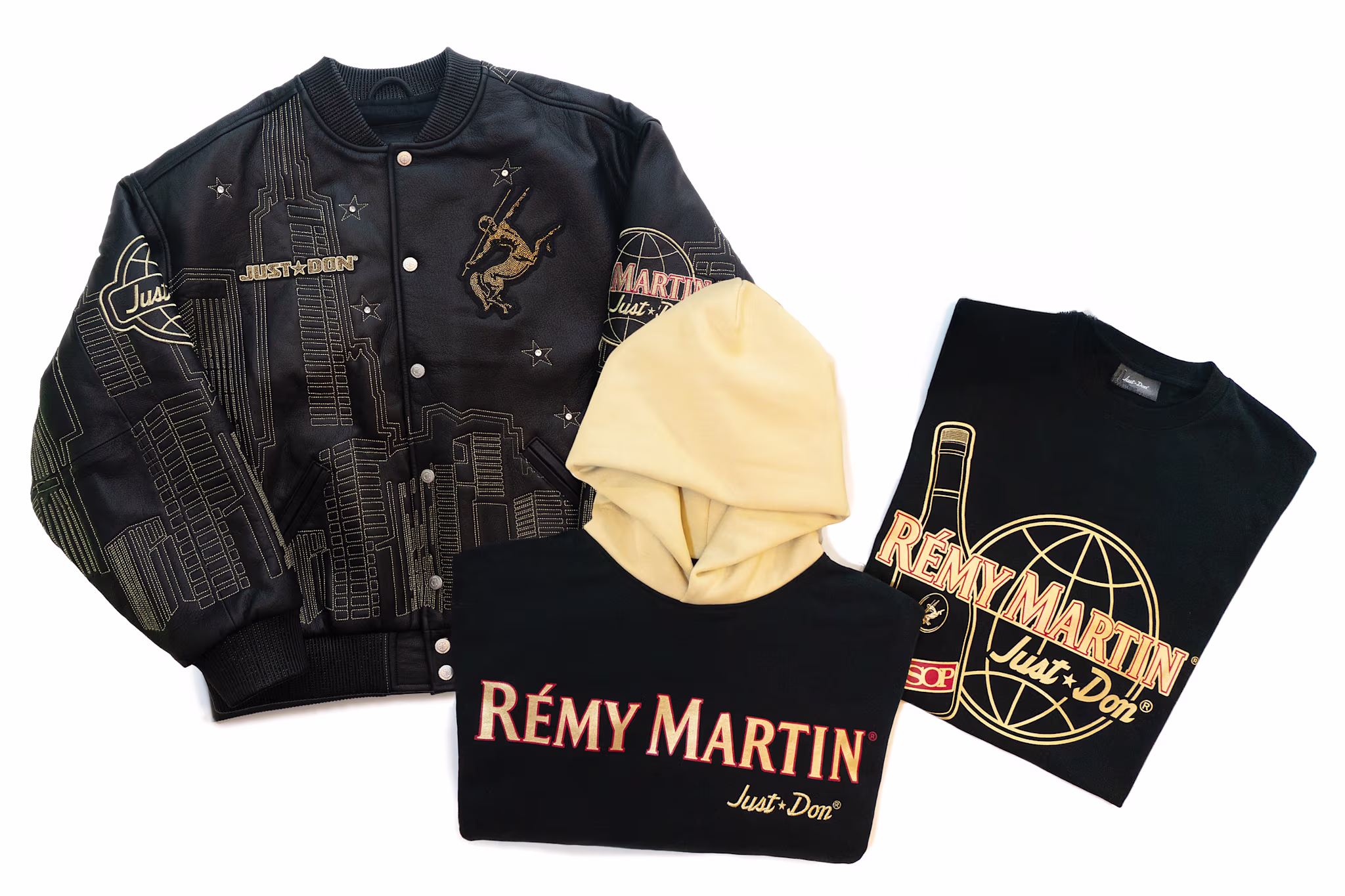 A black jacket, beige hoodie, and black T-shirt featuring Rémy Martin and Just Don branding with cityscape and bottle designs.