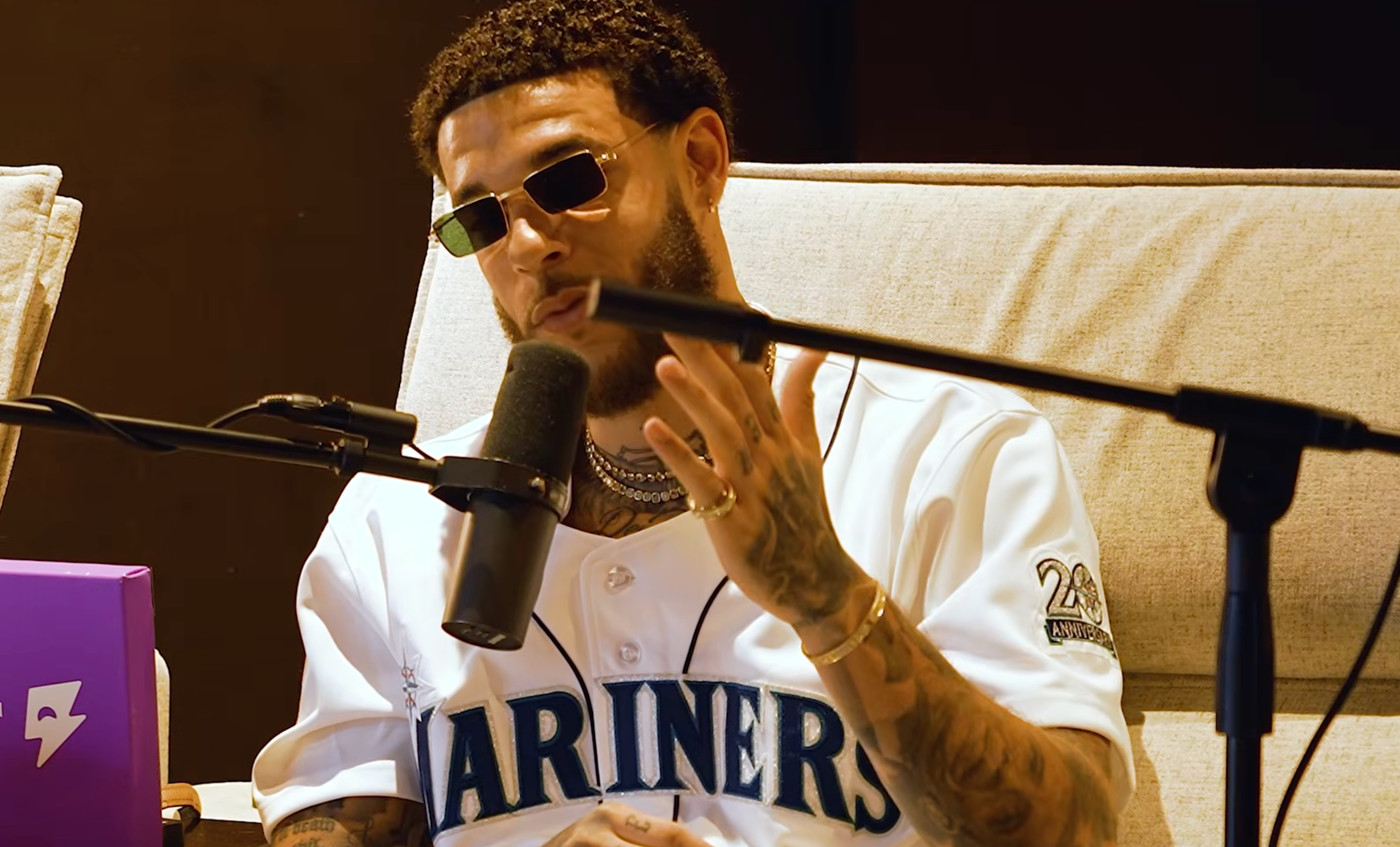 Lonzo Ball wearing sunglasses and a Seattle Mariners jersey speaks into a microphone during a podcast or interview.