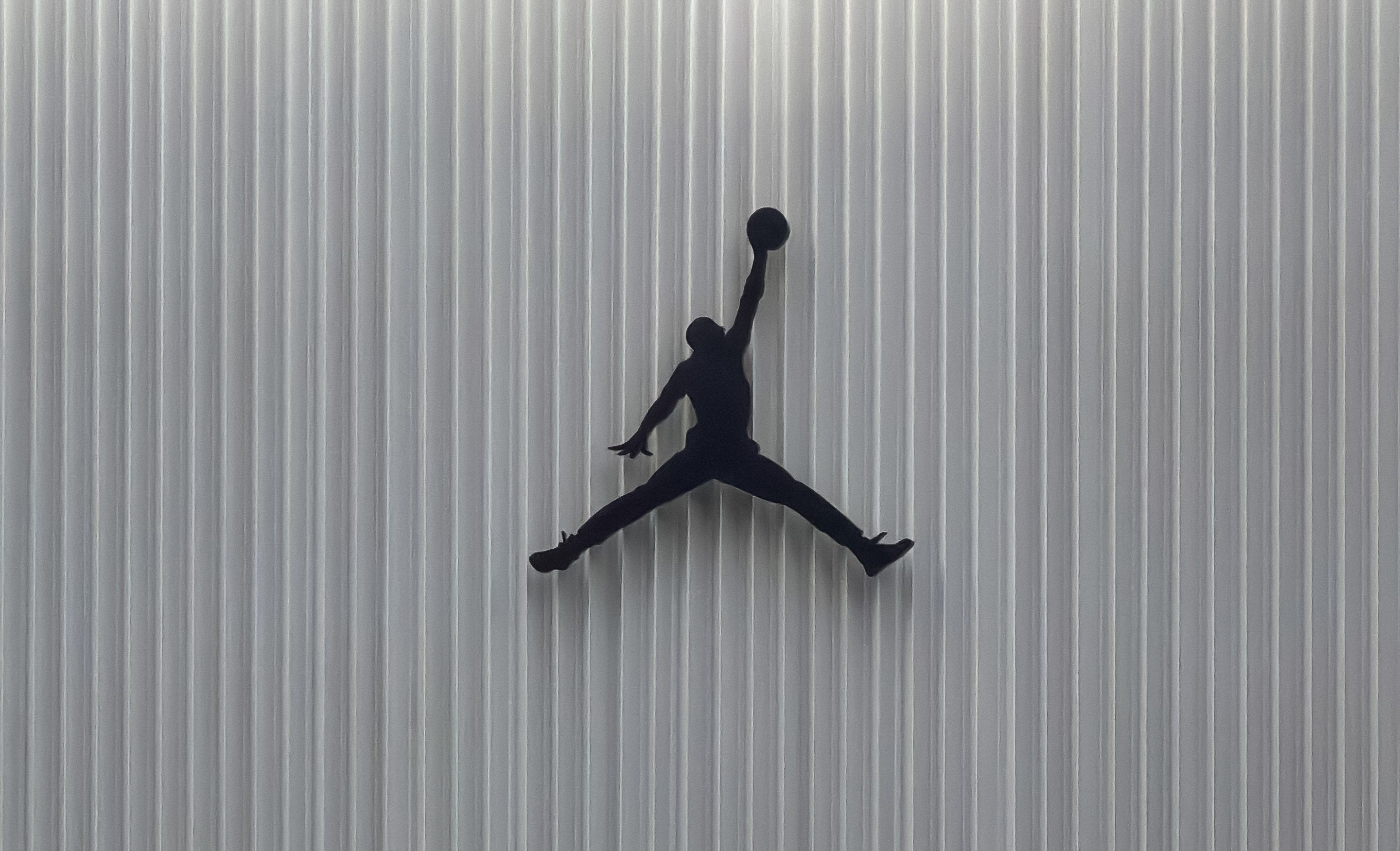 A store with the Jumpman logo on the facade, showcasing athletic apparel and sneakers in the window displays. People walk by outside.