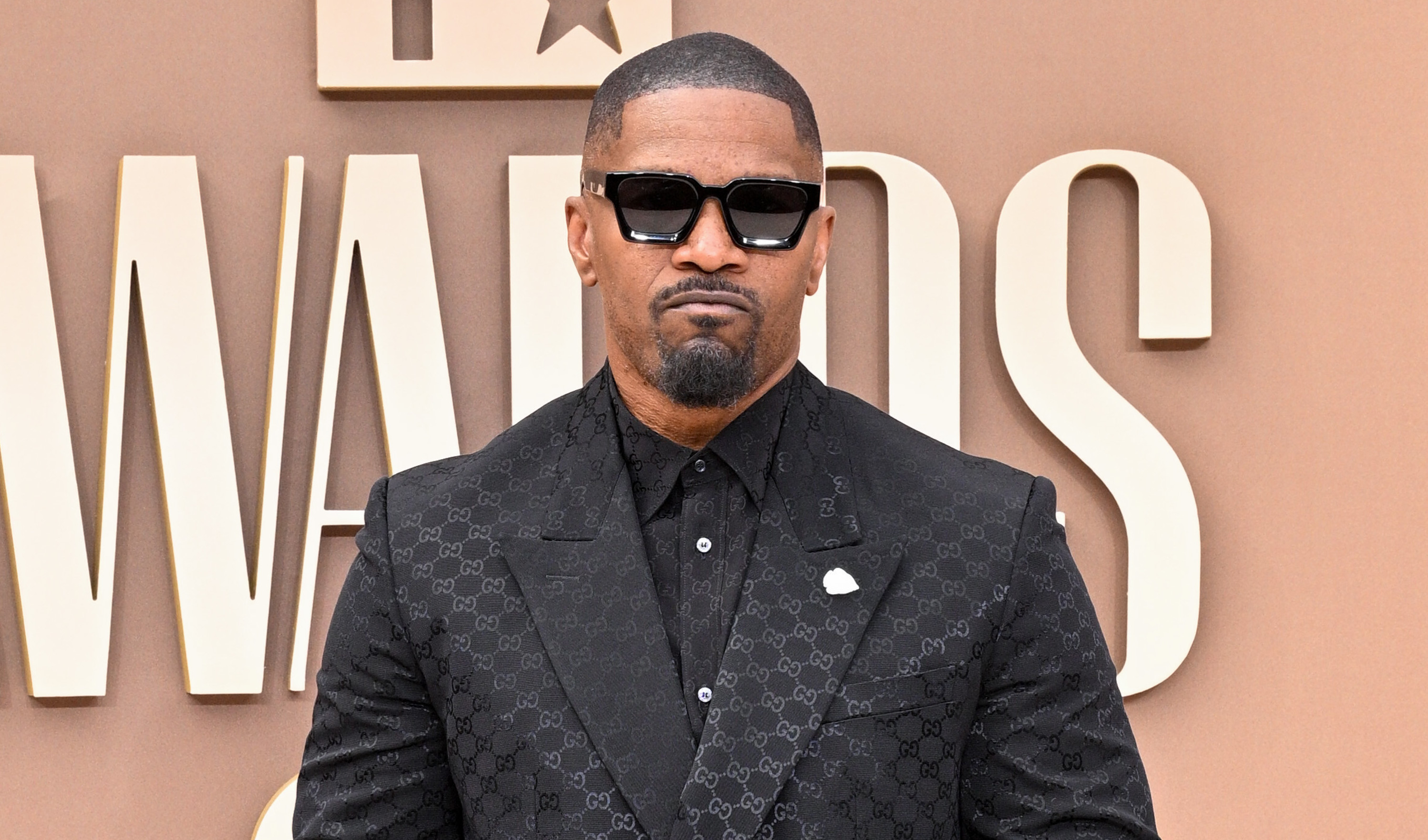 Jamie Foxx in a black suit and sunglasses stands confidently at the BET Awards, posing on the red carpet.