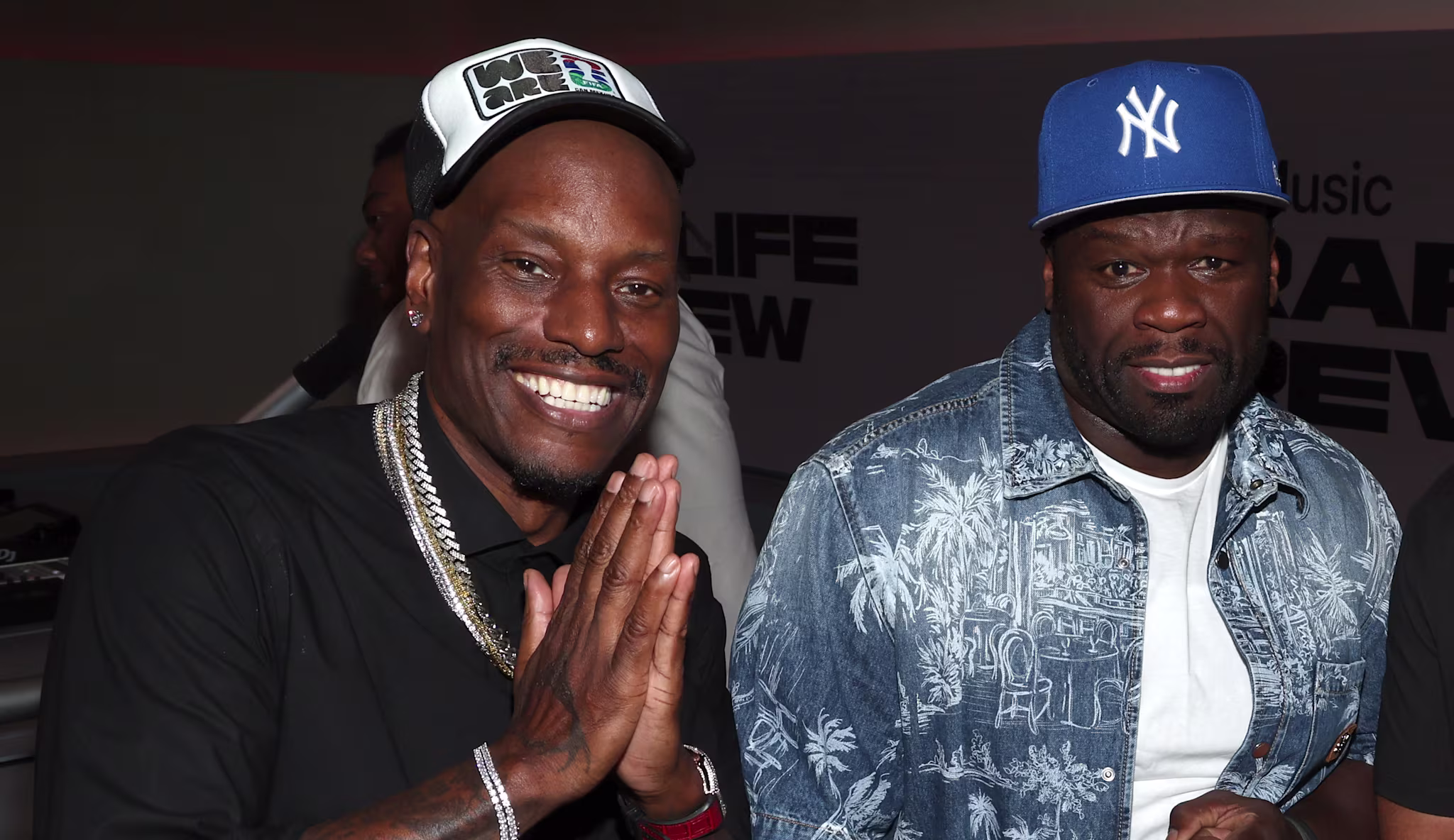Tyrese wears a black shirt and cap, 50 Cent a blue patterned shirt and blue cap.