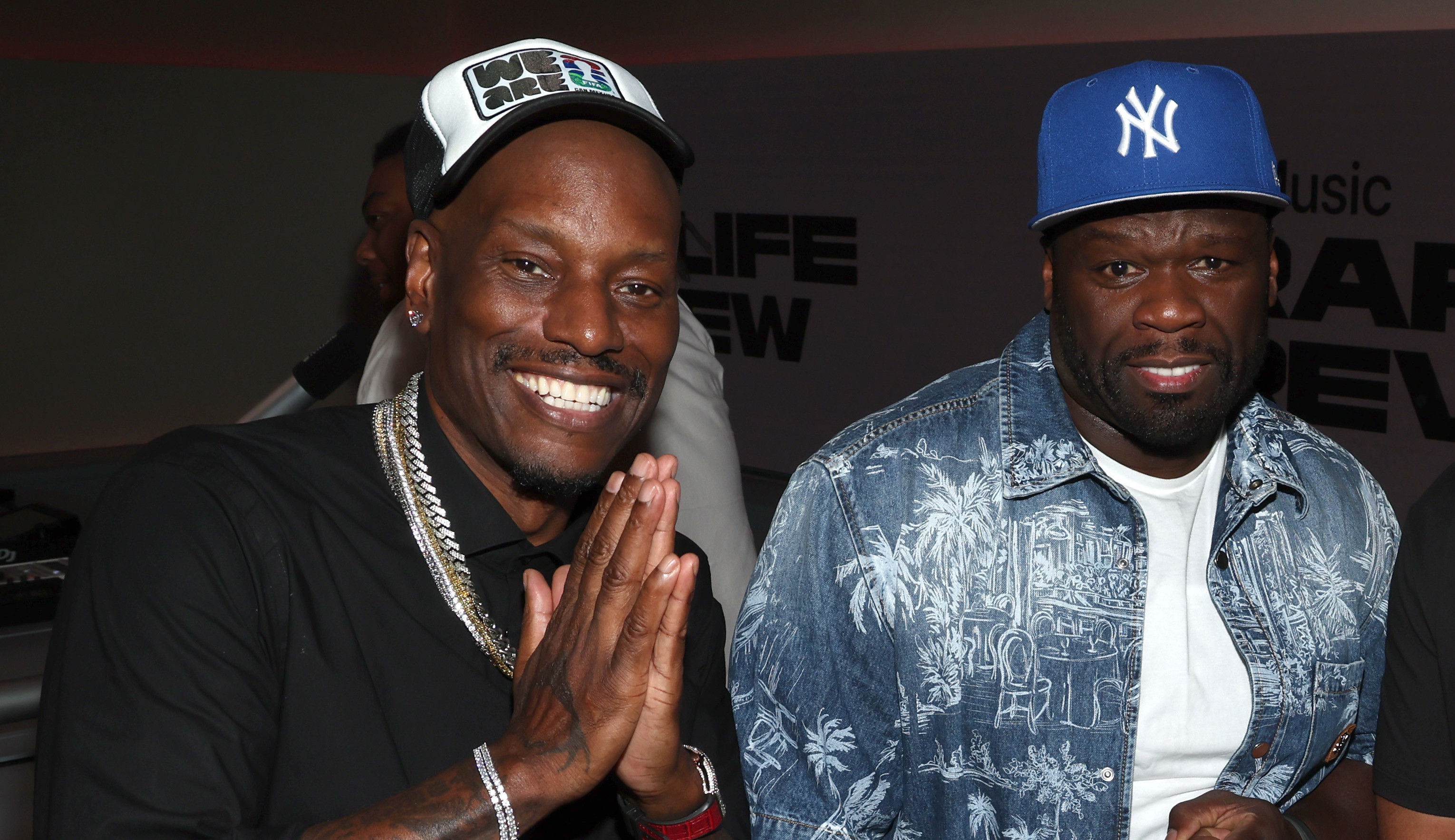Tyrese wears a black shirt and cap, 50 Cent a blue patterned shirt and blue cap.