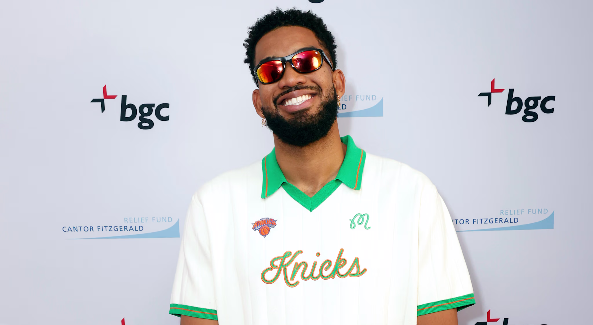 Karl-Anthony Towns in a Knicks shirt and sunglasses, smiling on a red carpet with a BGC backdrop.