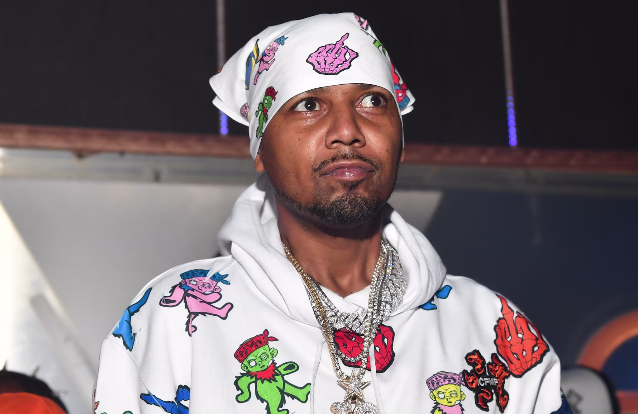 Juelz Santana wearing a colorful hoodie with cartoon designs and a matching bandana, accessorized with multiple necklaces.